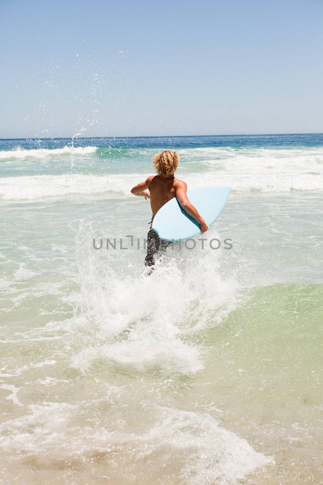 Young blonde man wading in the water while holding his blue surfboard