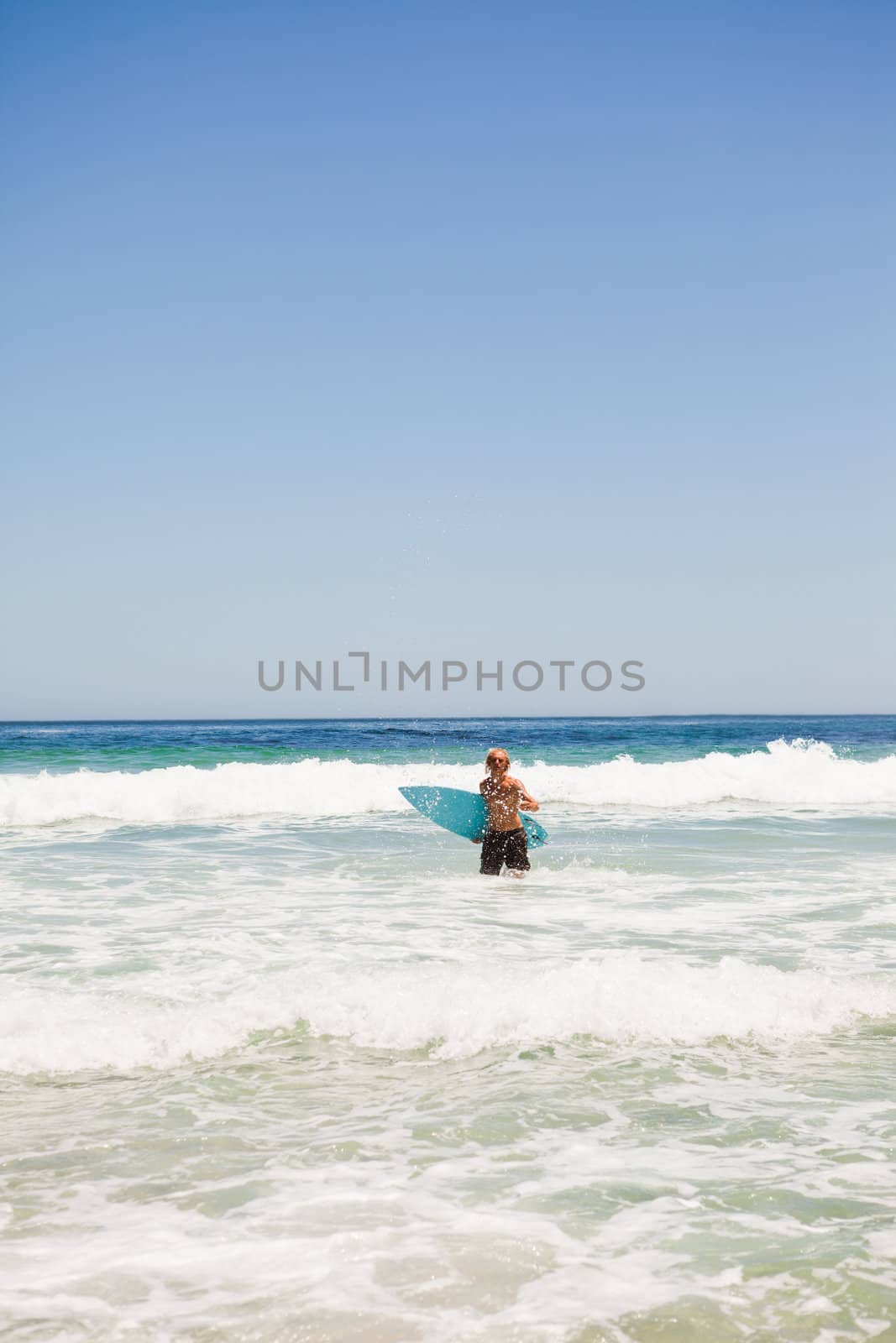 Young blonde man returning to the beach while holding his surfboard