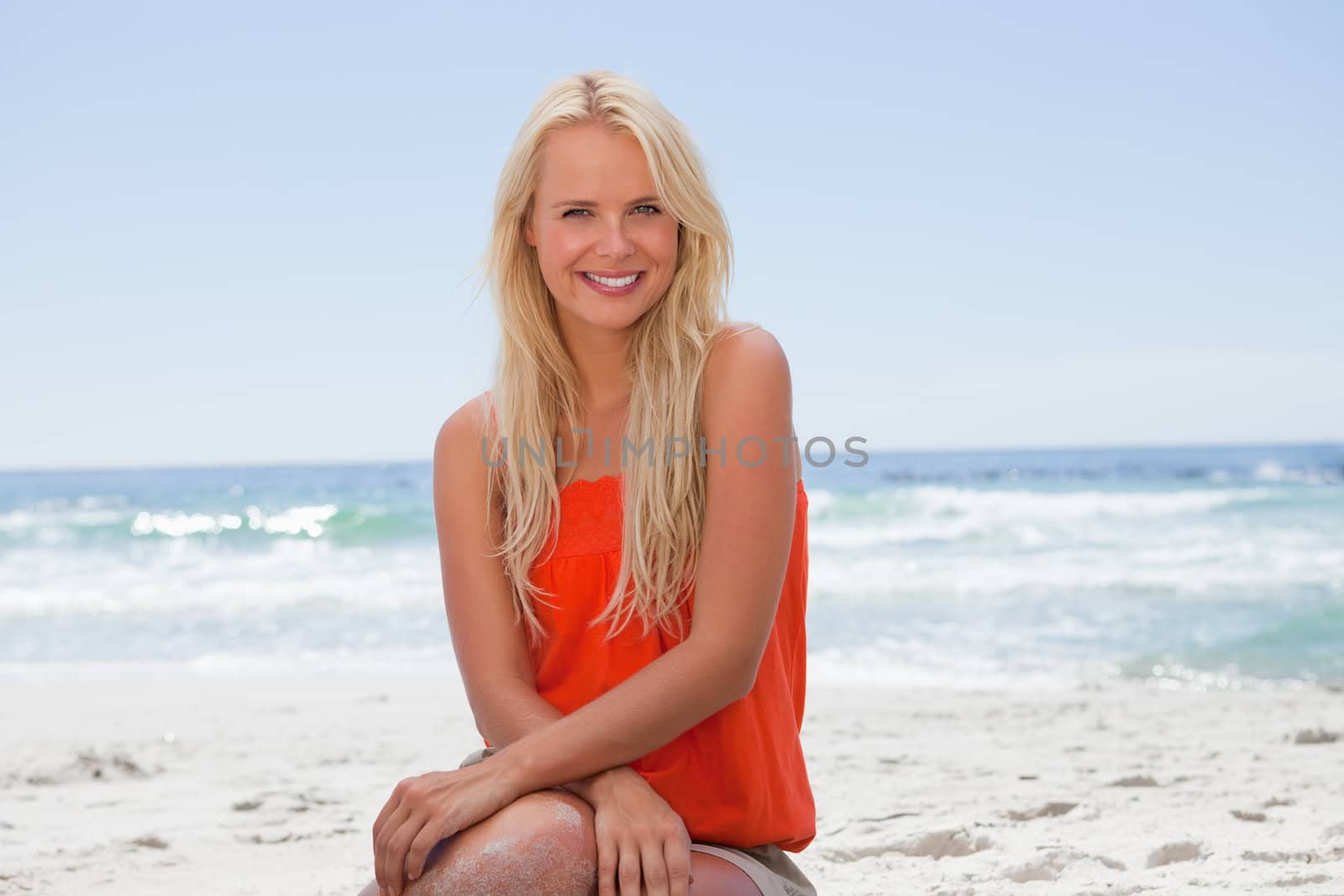 Young woman sitting down in front of the ocean while showing a great smile