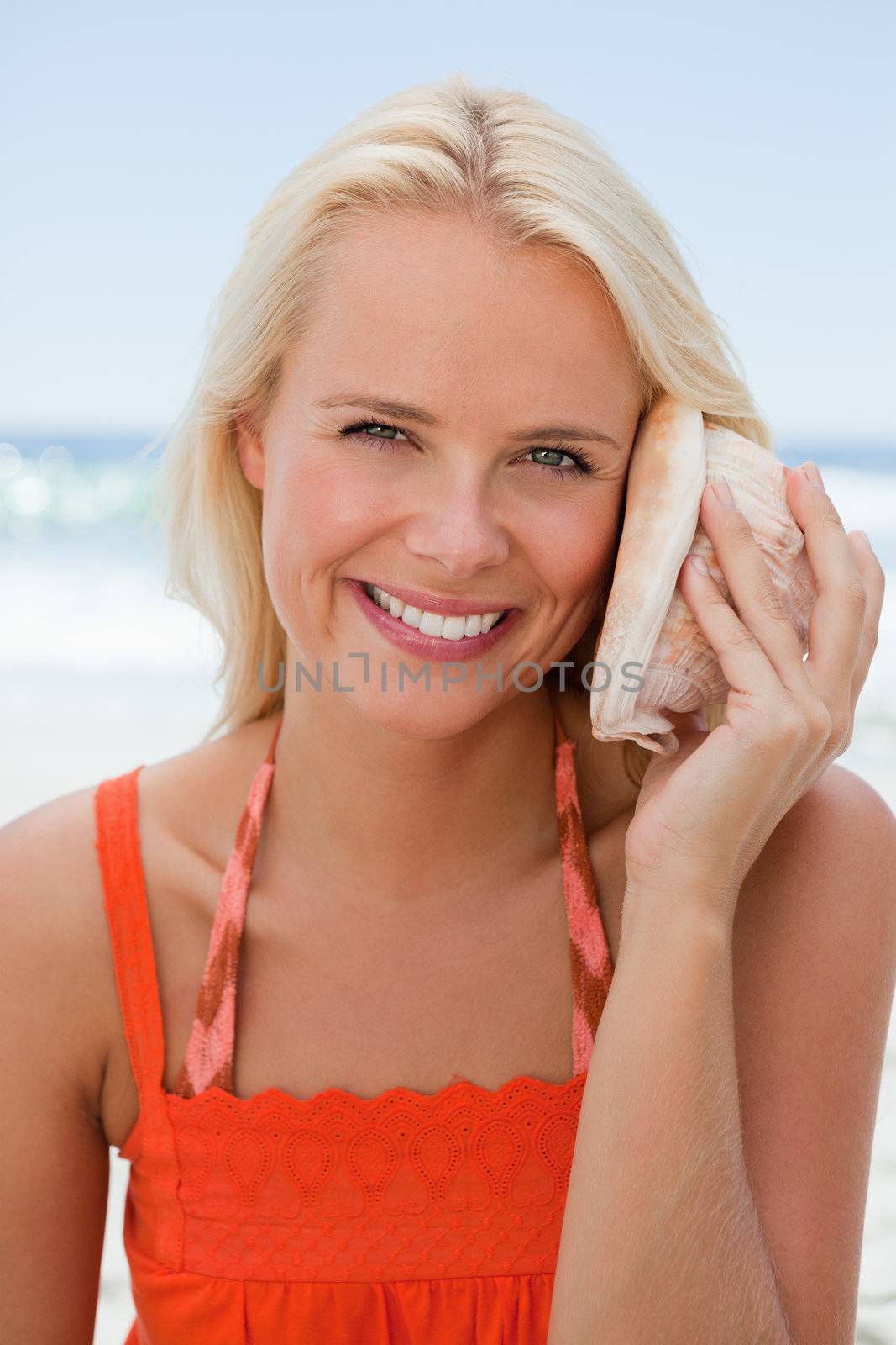 Young smiling woman holding a shell to hear the sound of the sea by Wavebreakmedia