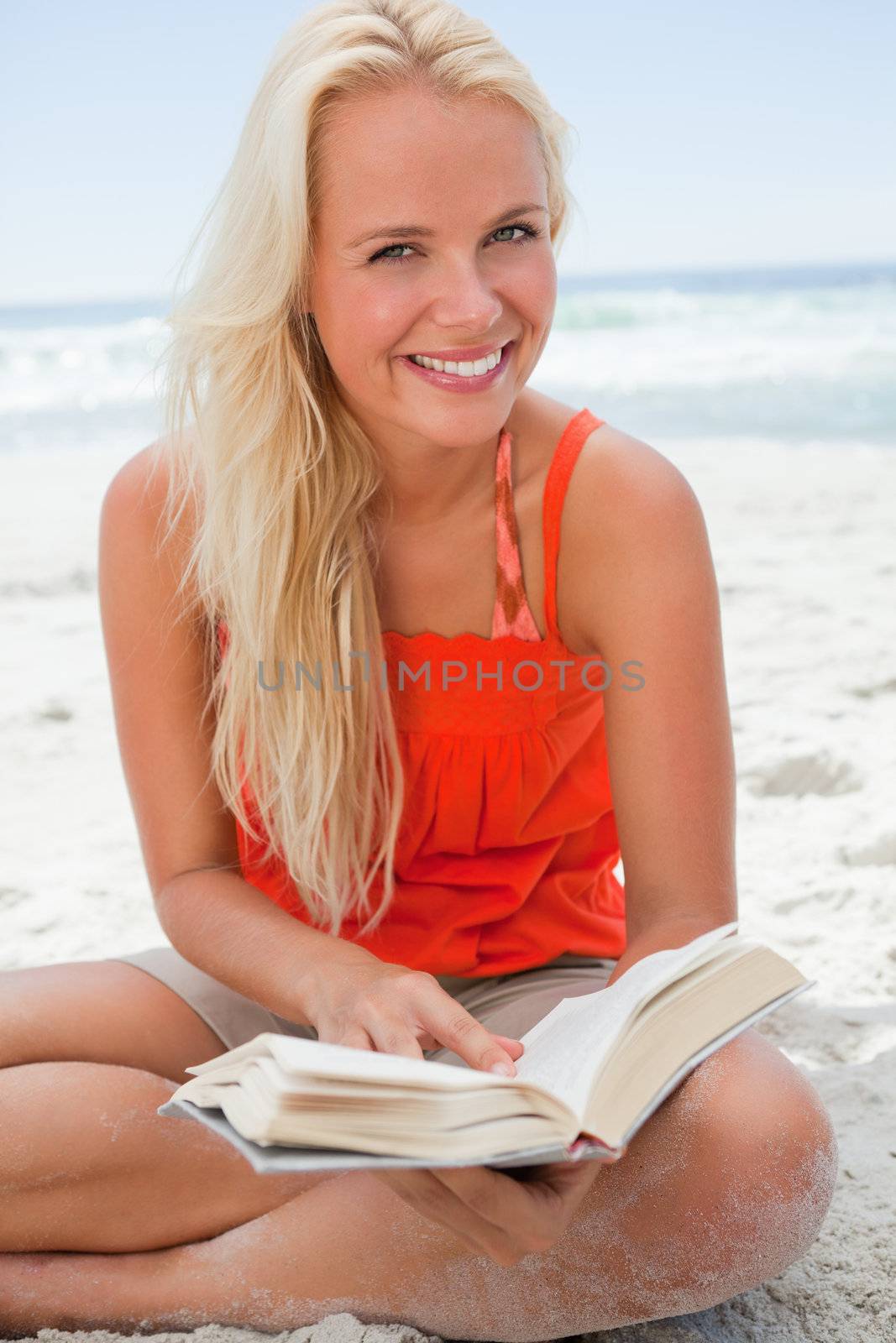 Young smiling blonde woman looking at the camera while reading a book