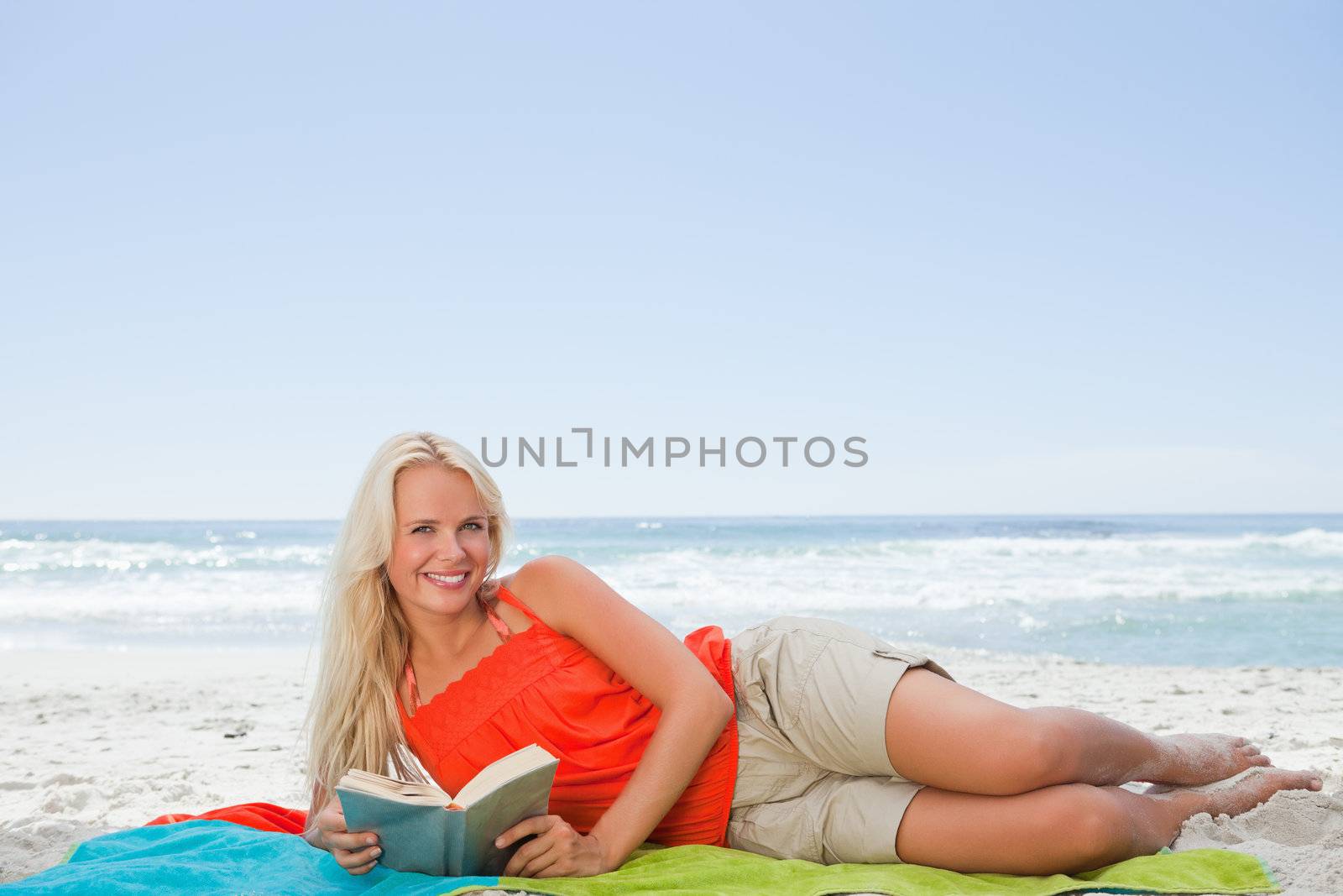 Young woman lying on the side while looking at the camera and holding a book