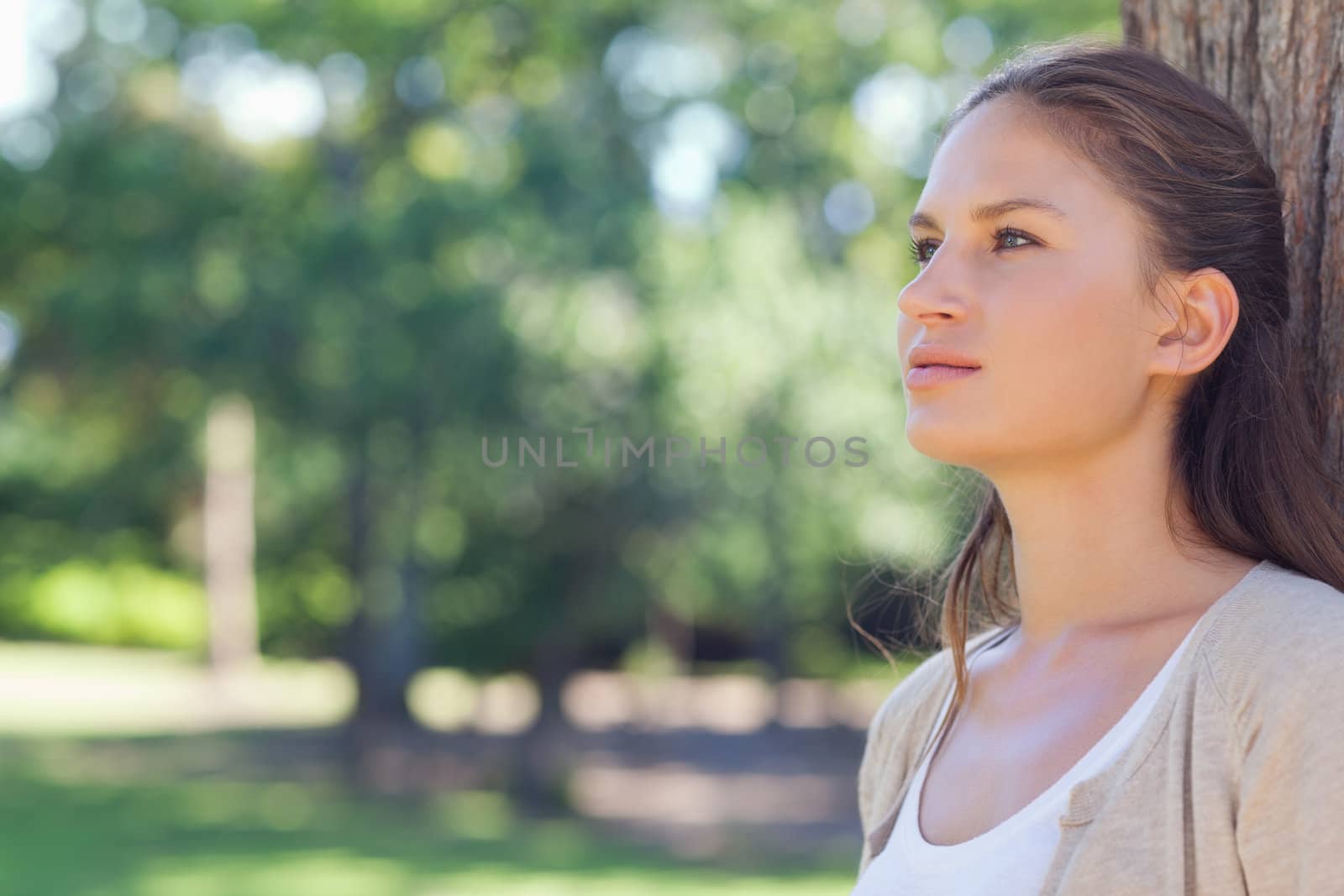 Woman standing with her back against a tree by Wavebreakmedia