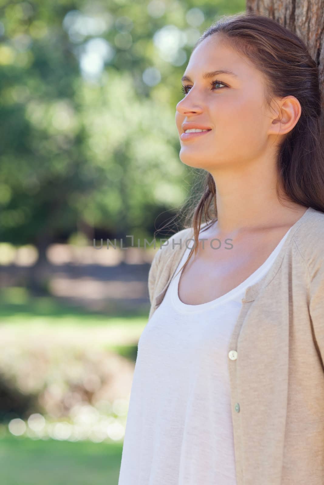 Smiling young woman leaning against a tree in the park