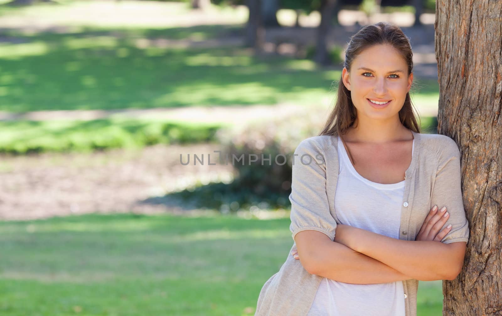 Smiling woman with her arms folded and leaning against a tree by Wavebreakmedia