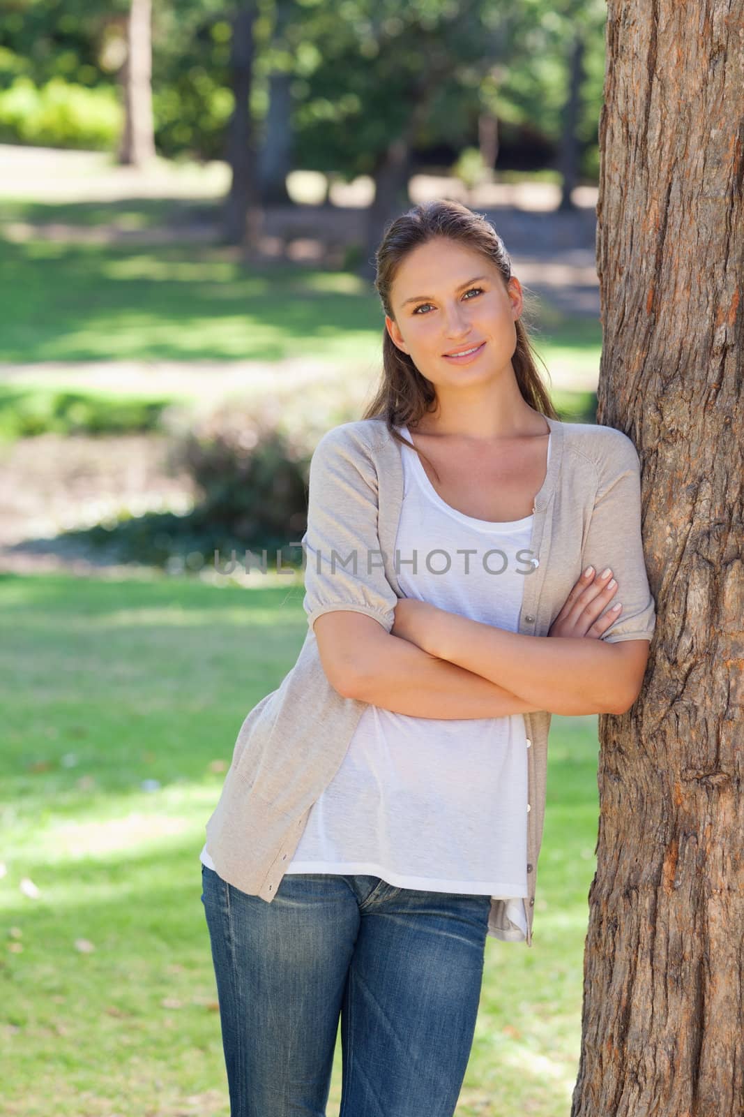 Smiling young woman with her arms folded leaning against a tree