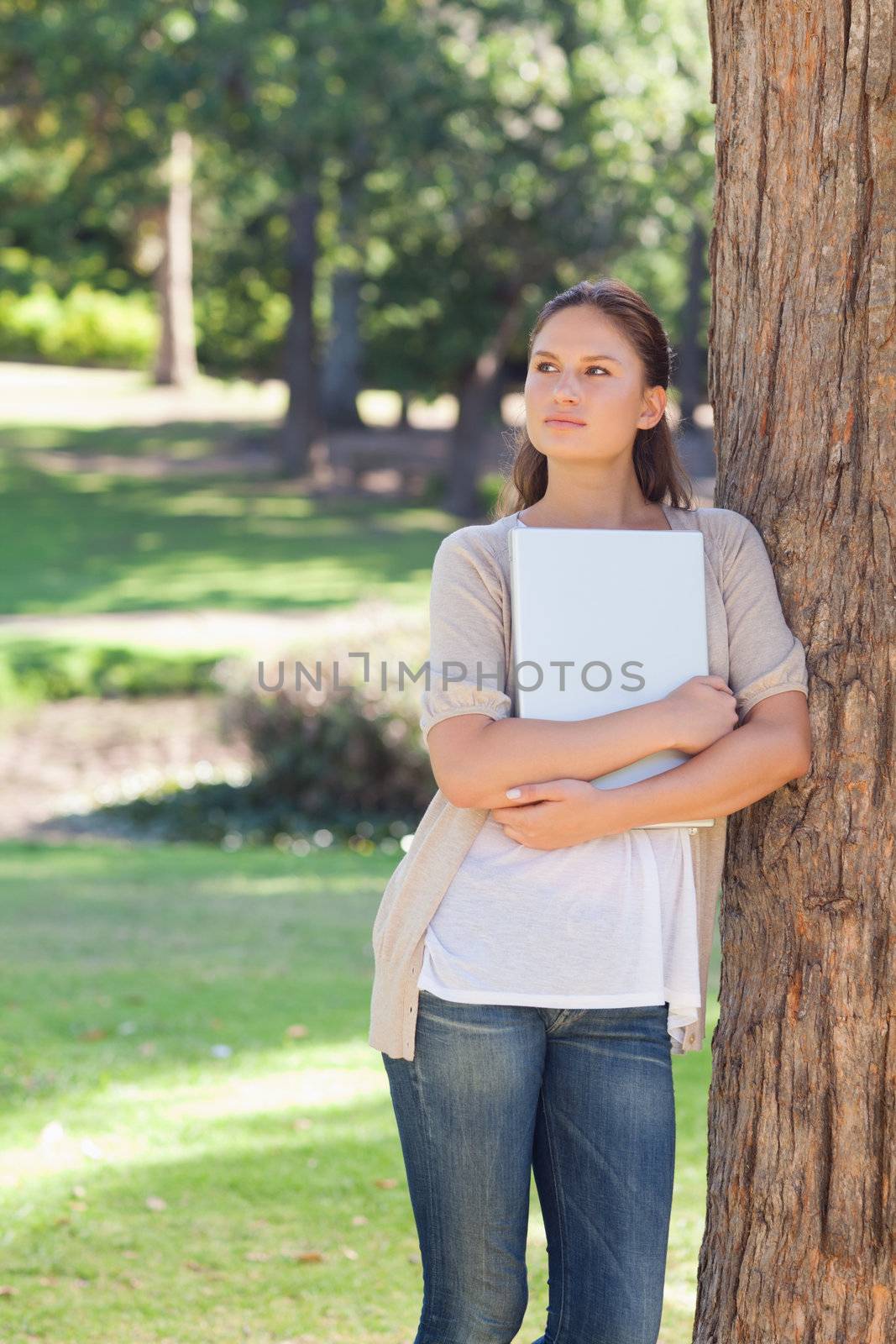 Woman with a laptop leaning against a tree by Wavebreakmedia