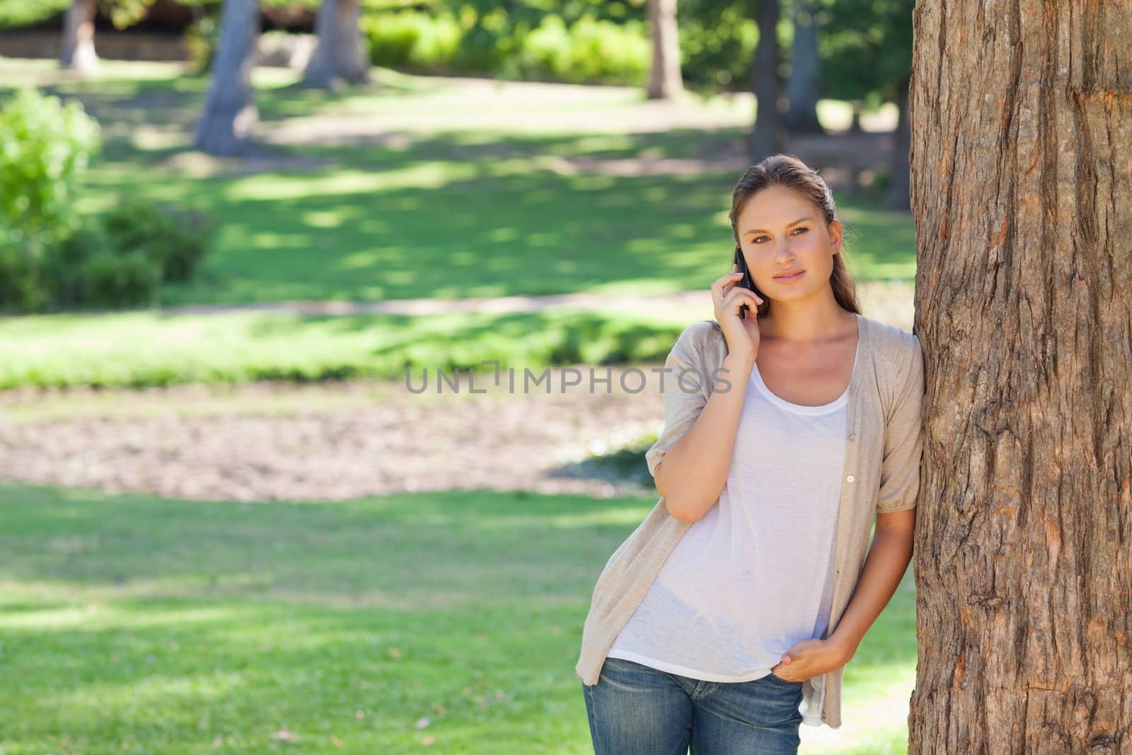 Young woman on the phone leaning against a tree