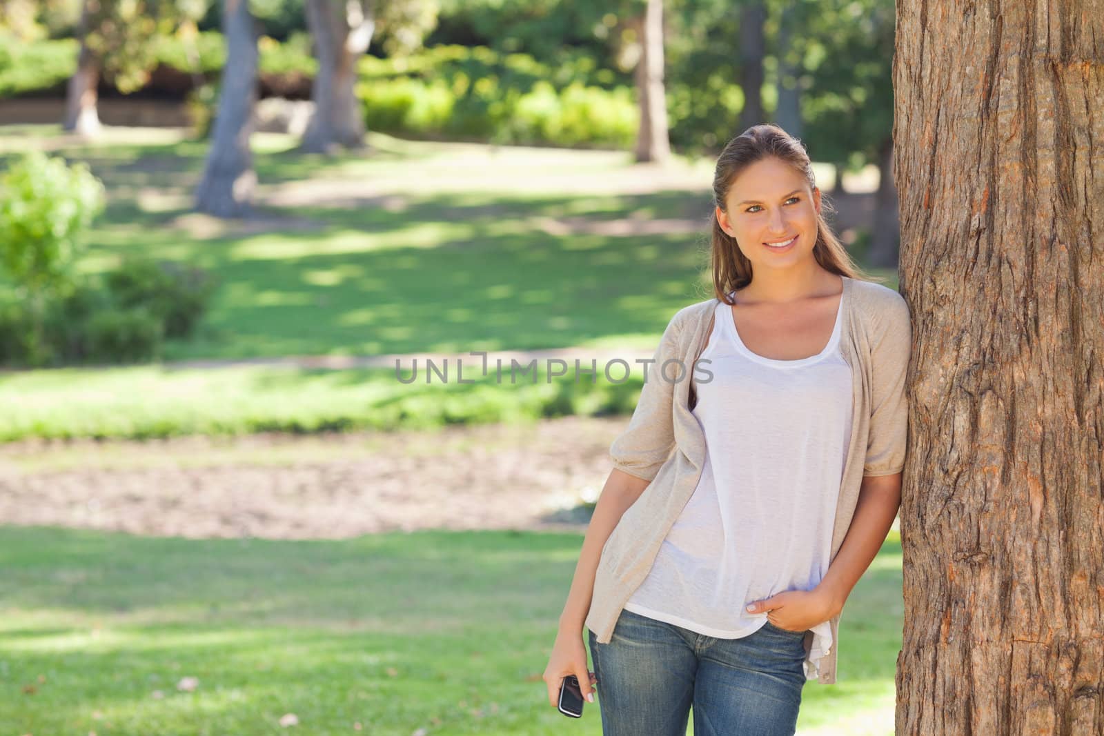 Woman with a cellphone leaning against a tree by Wavebreakmedia