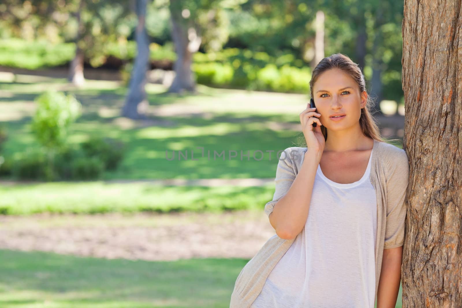 Woman on the cellphone leaning against a tree by Wavebreakmedia