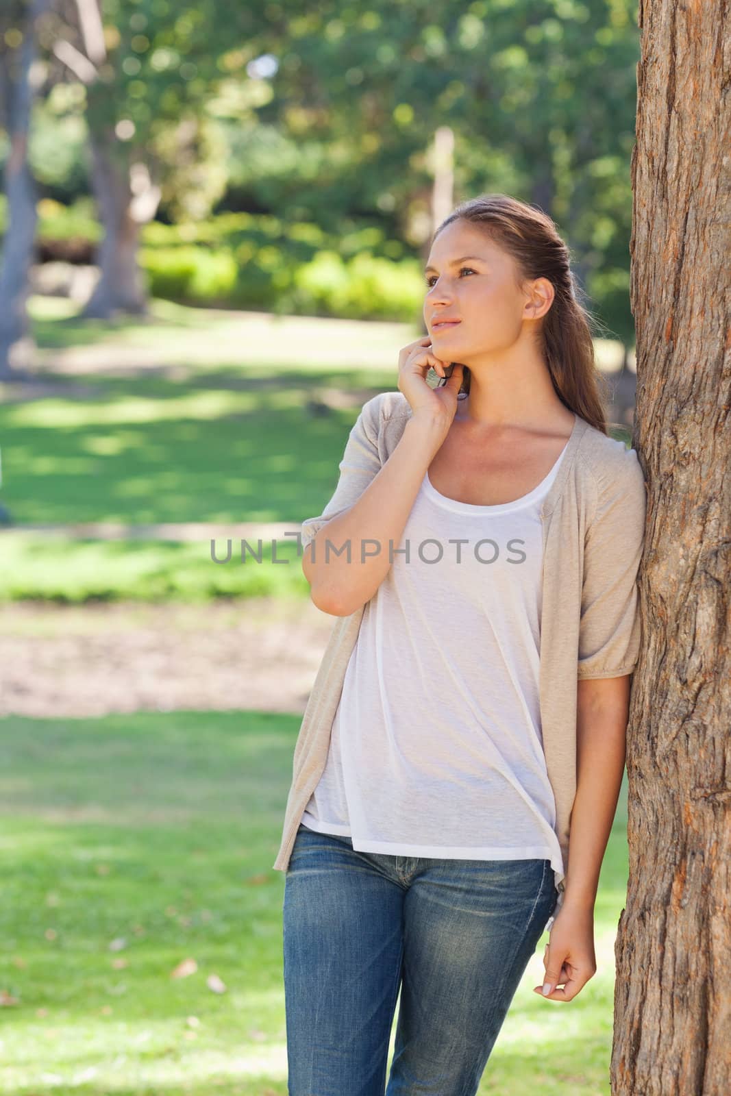 Woman talking on the phone while leaning against a tree by Wavebreakmedia