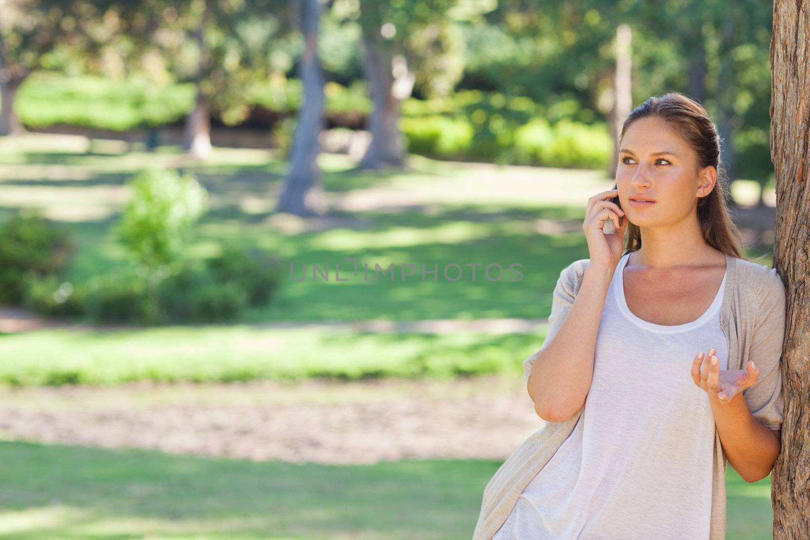 Young woman talking on her cellphone while leaning against a tree