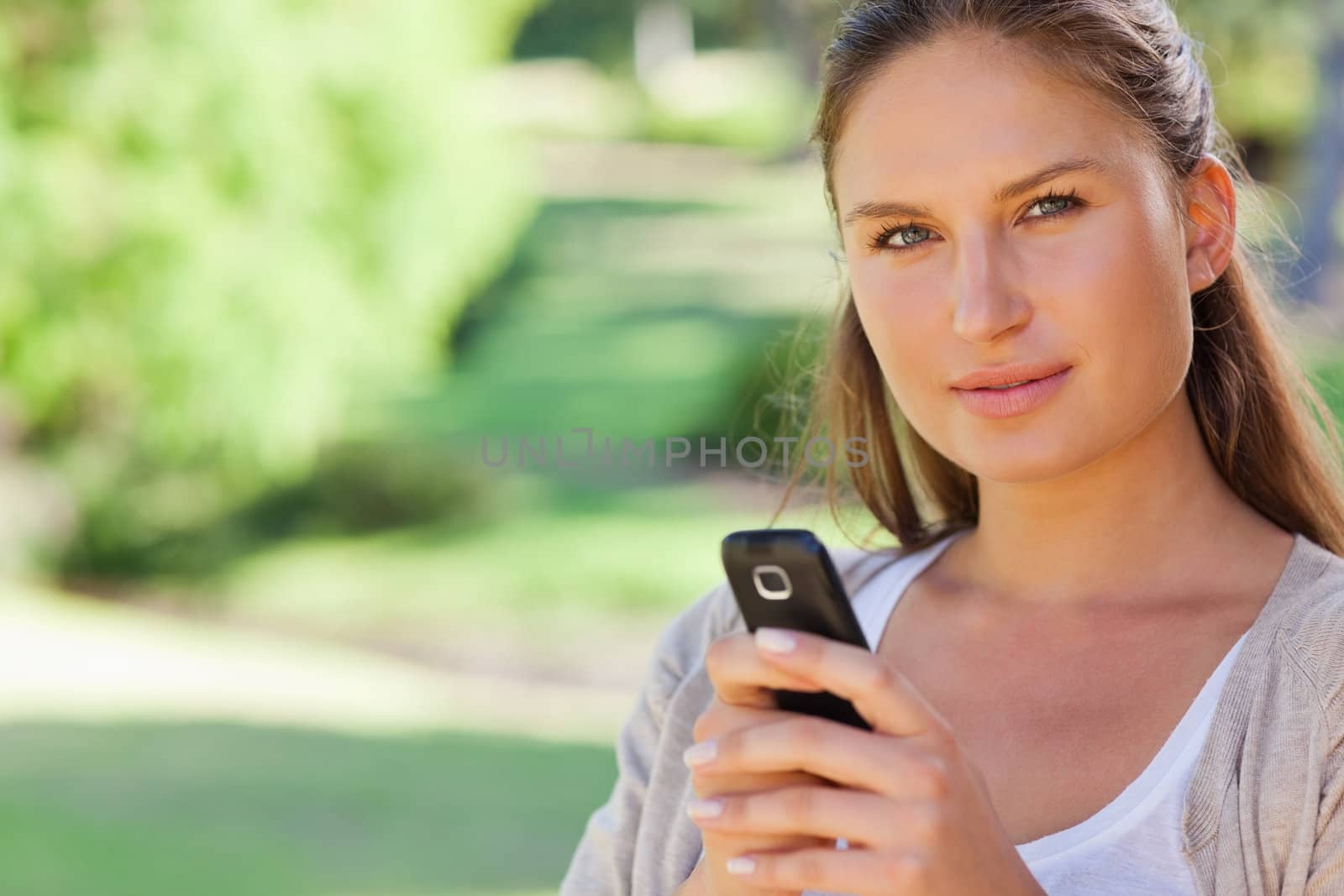 Close up of young woman holding her mobile phone in the park