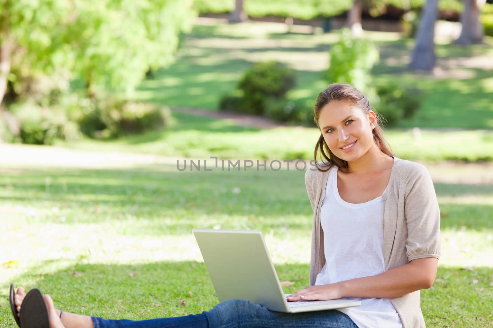 Smiling young woman sitting on the grass with her laptop