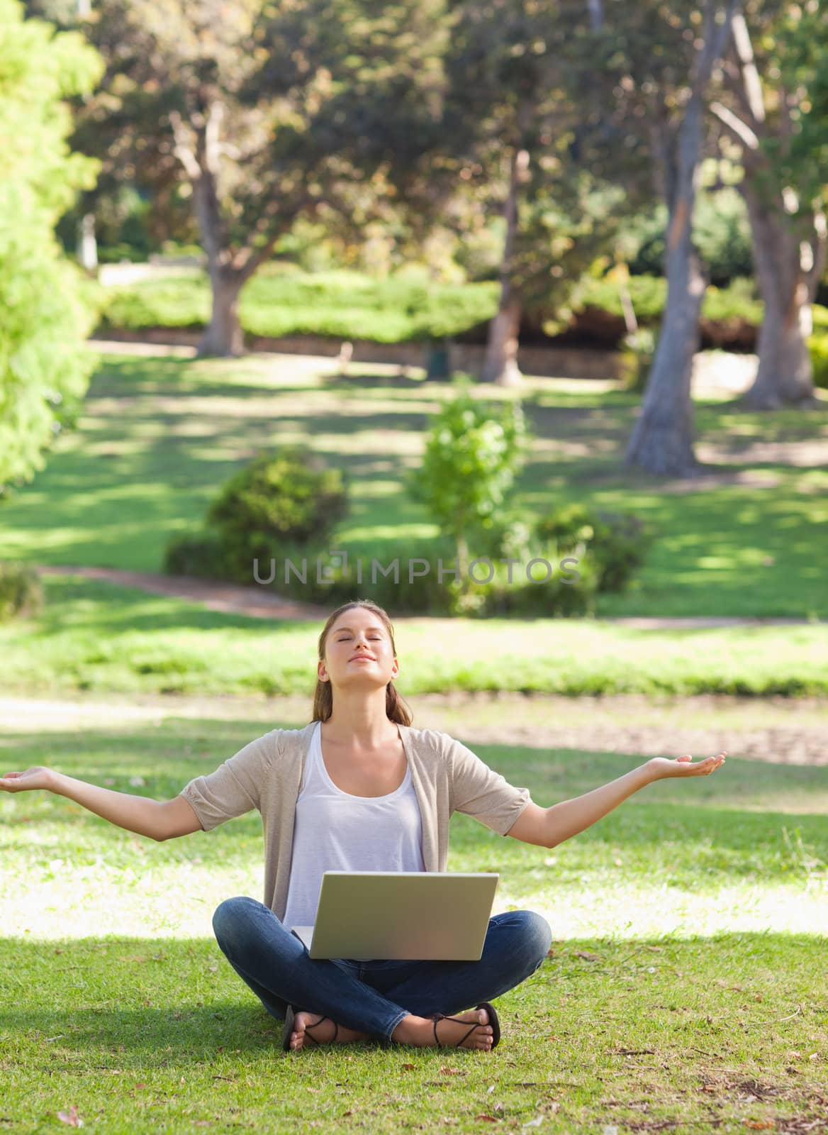 Young woman sitting on the lawn in a yoga position with a laptop