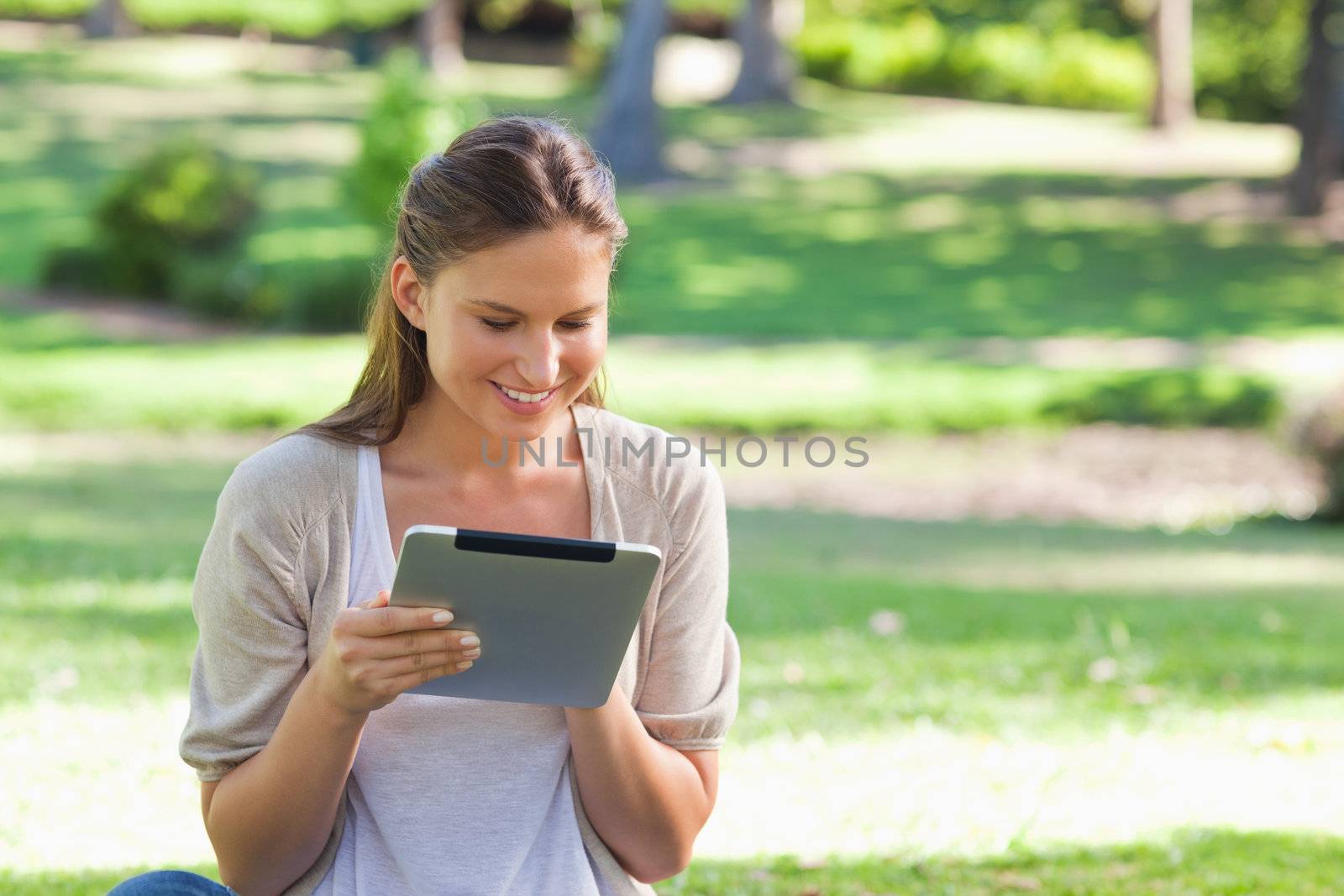 Smiling woman with her tablet computer sitting on the lawn by Wavebreakmedia