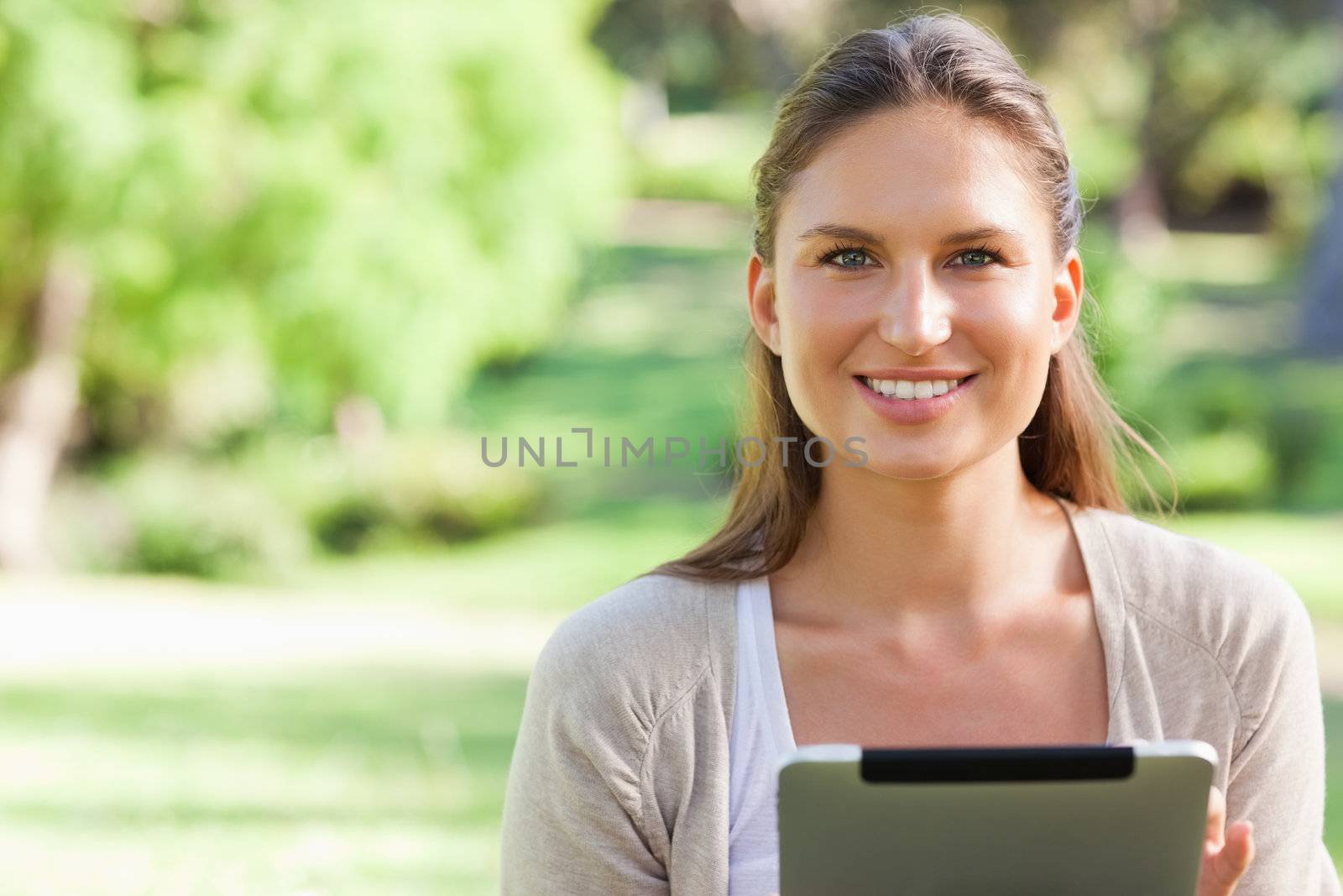 Smiling young woman sitting on the lawn with a tablet computer