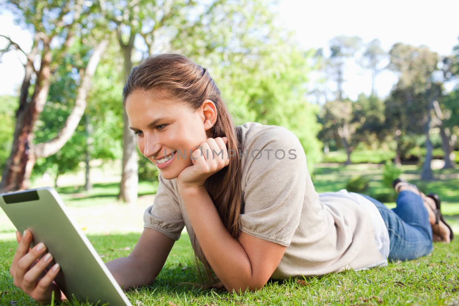 Smiling woman laying on the lawn with her tablet computer by Wavebreakmedia