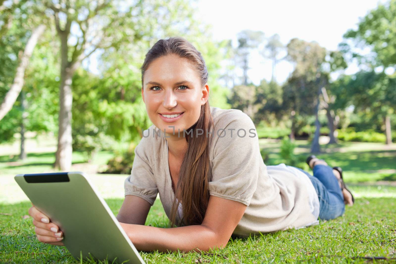 Smiling young woman with her tablet computer lying on the lawn