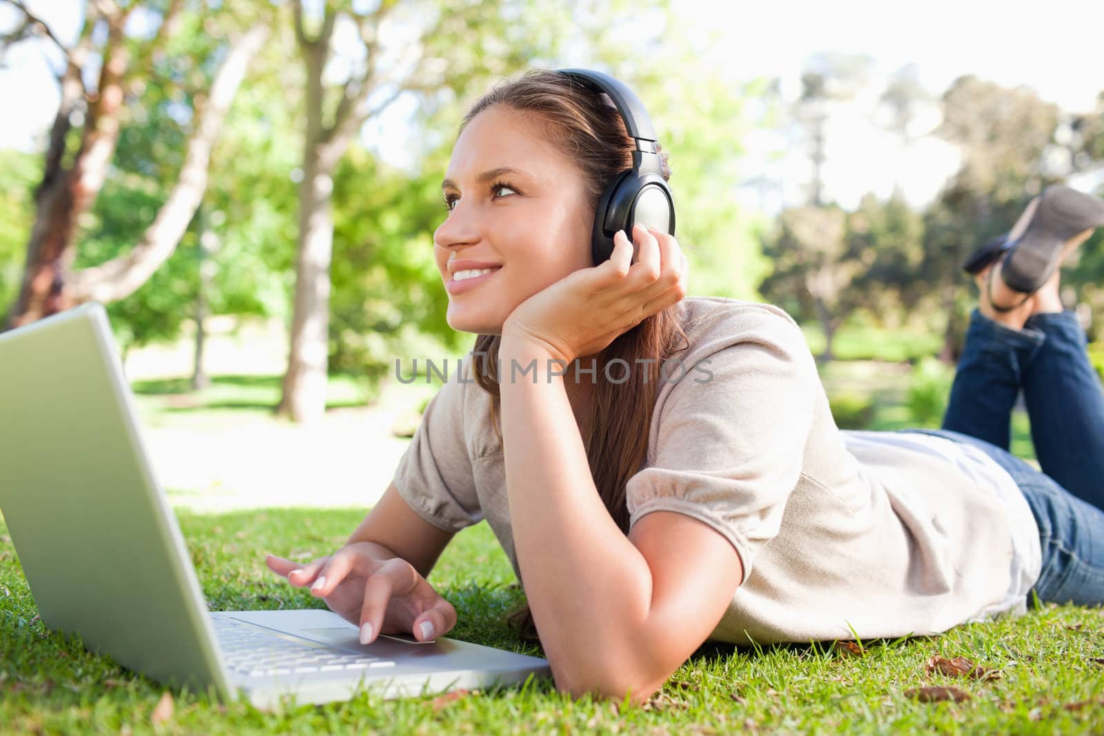 Smiling young woman with headphones and a laptop lying on the lawn