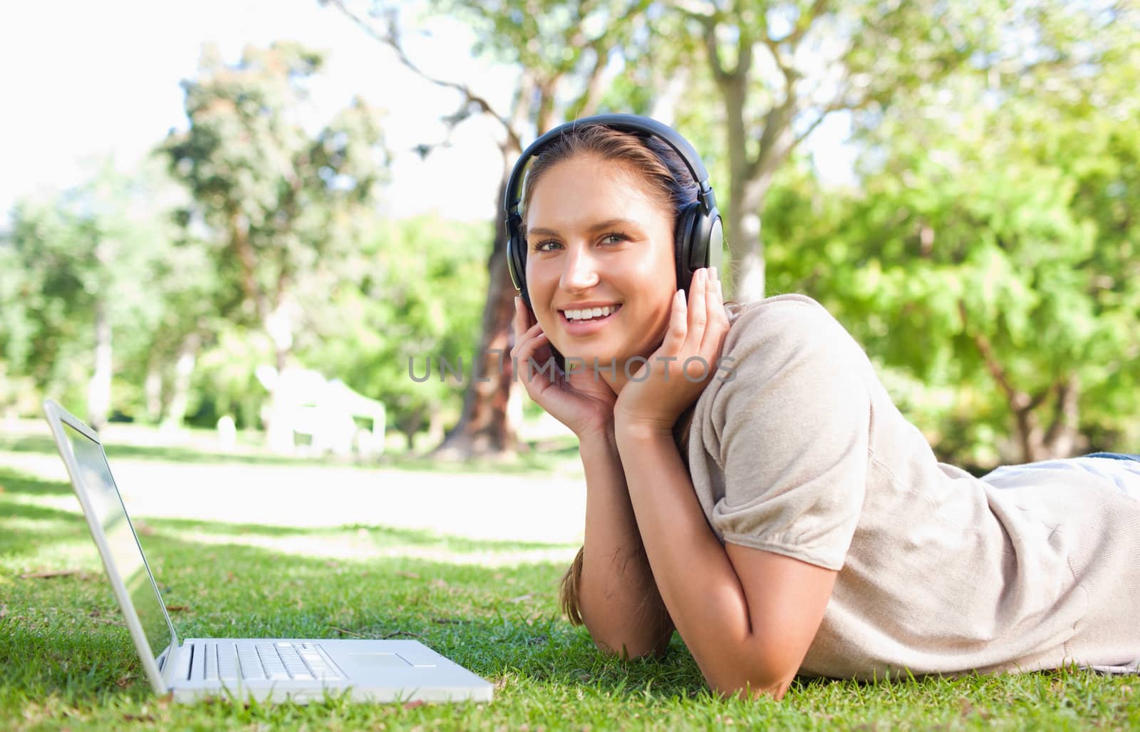 Young woman with a laptop and headphones lying on the lawn