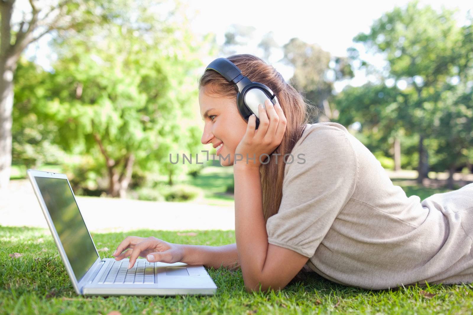 Side view of a woman with headphones and a laptop on the lawn by Wavebreakmedia