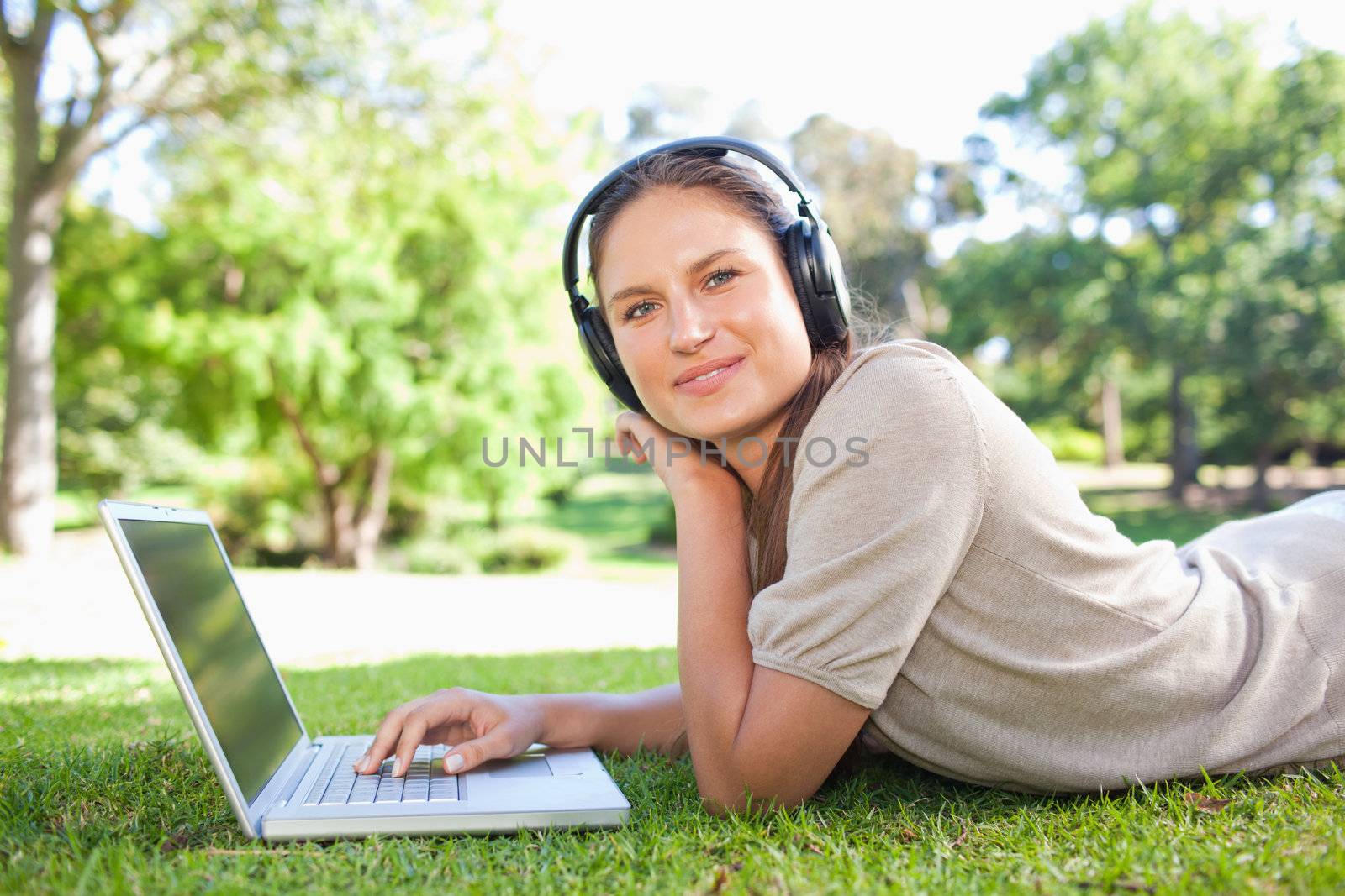 Side view of a young woman with her laptop and headphones lying on the lawn