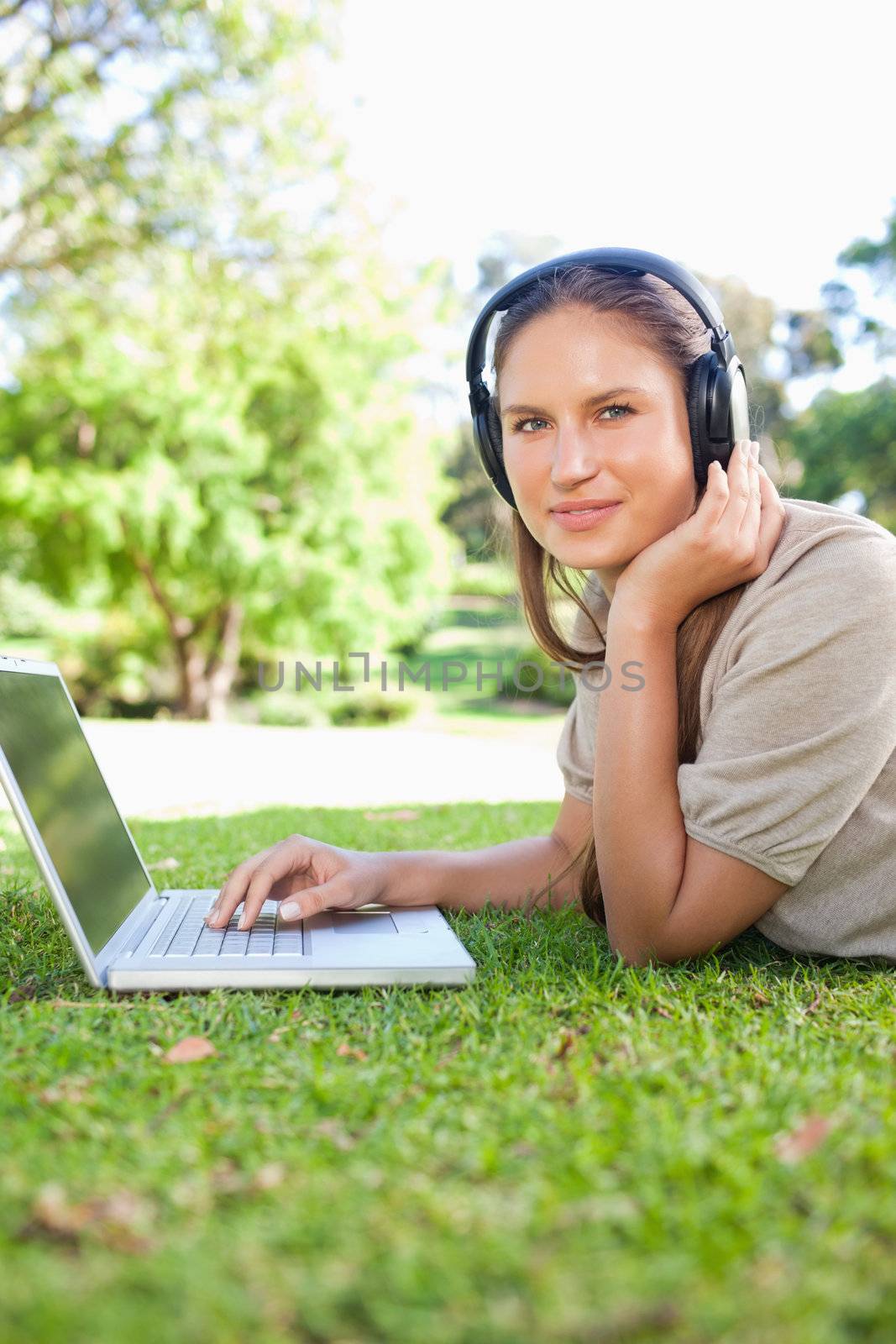 Side view of a woman lying on the lawn with laptop and headphones by Wavebreakmedia