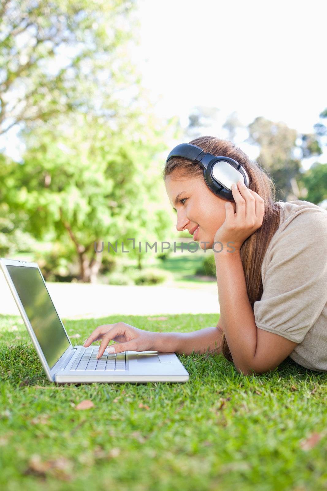 Side view of a young woman with a laptop and headphones on the lawn
