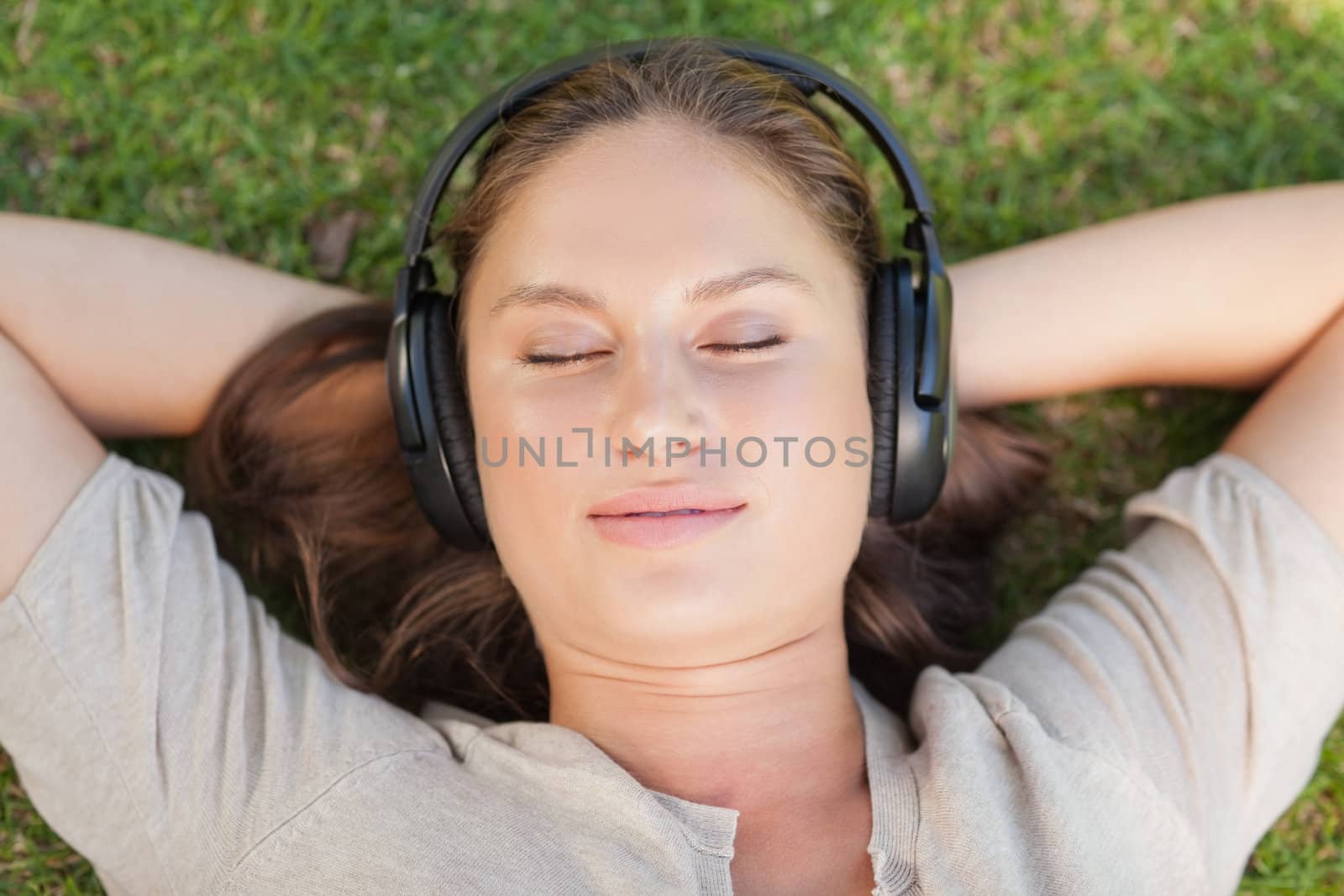 Relaxed woman lying on the lawn while listening to music by Wavebreakmedia