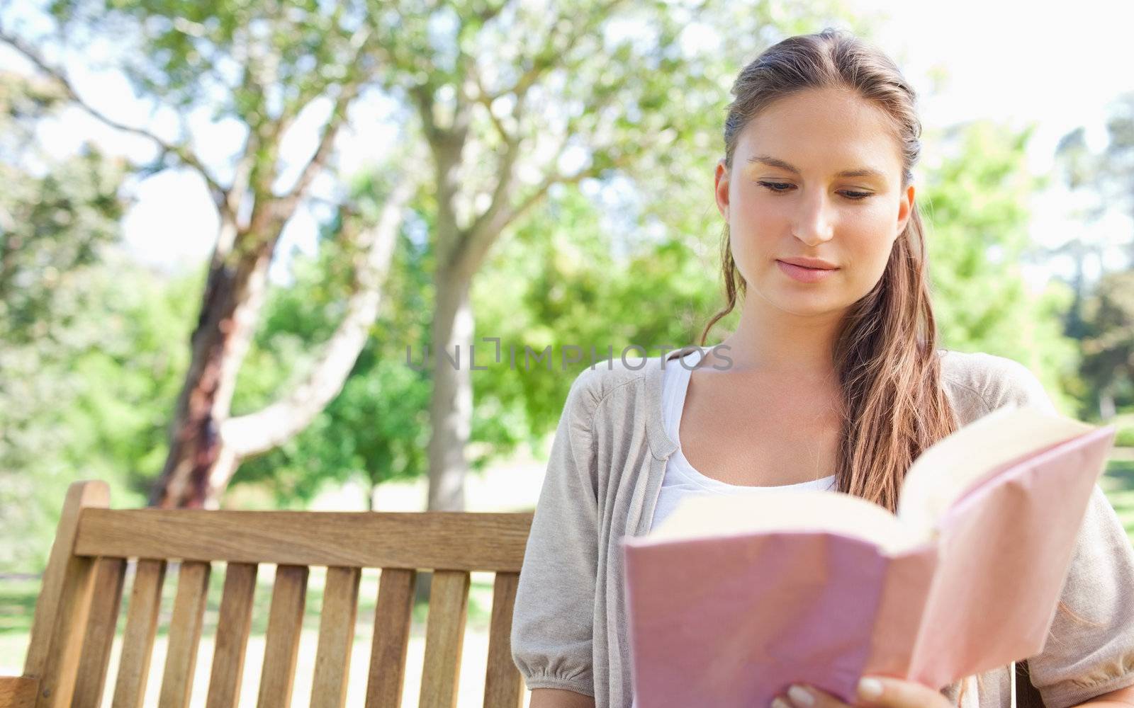 Young woman sitting on a park bench wihle reading a book