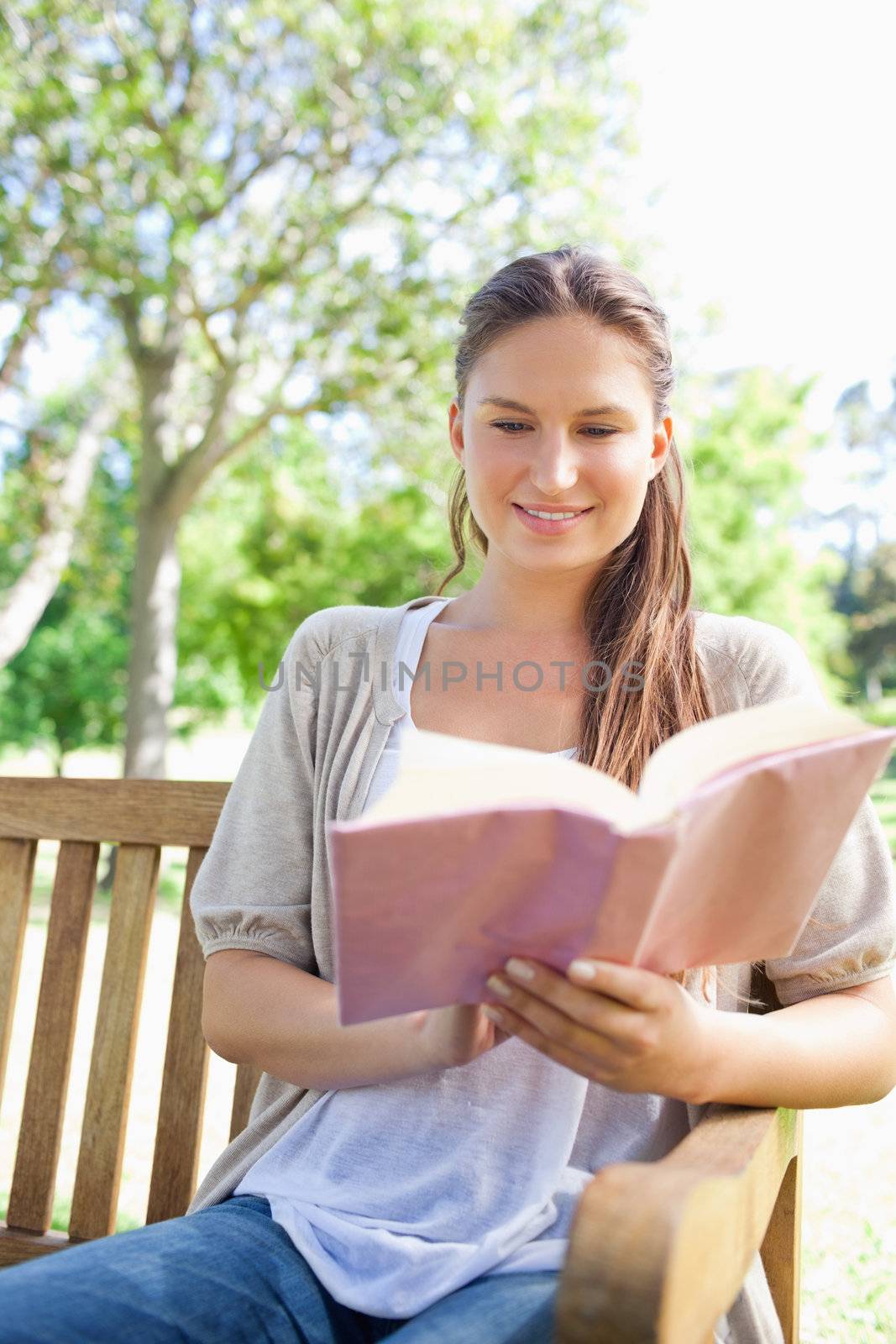 Smiling woman reading her book on a park bench by Wavebreakmedia