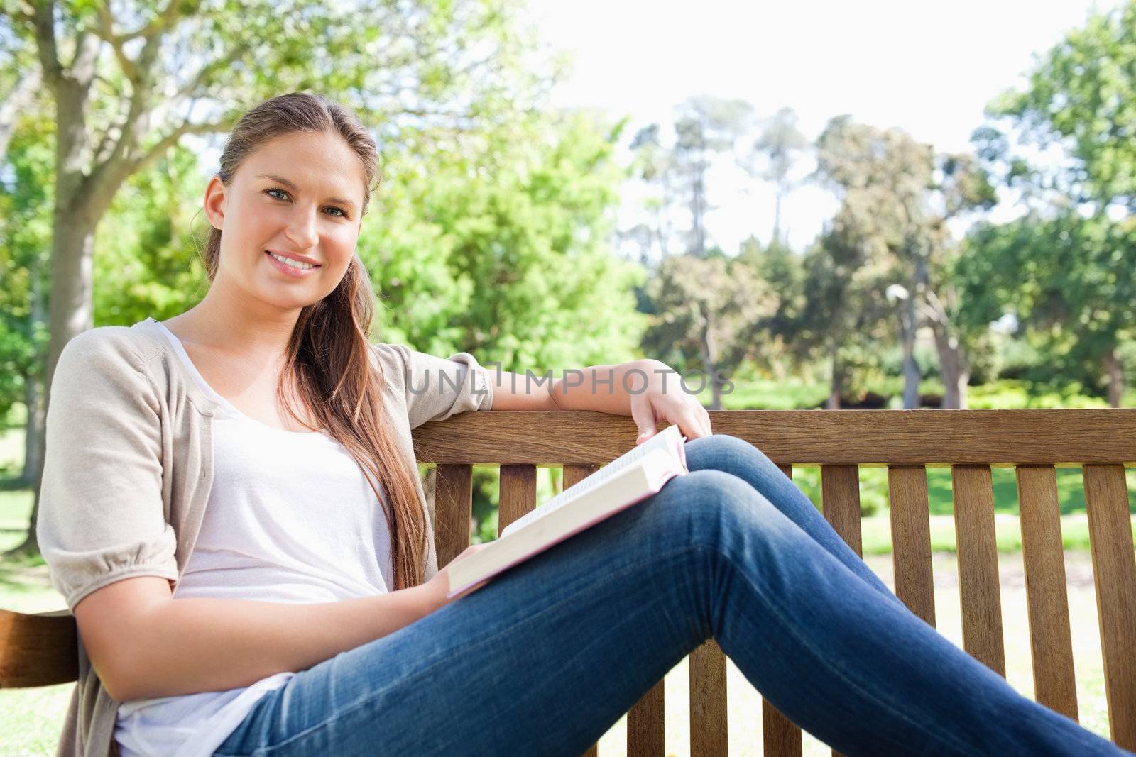 Smiling young woman sitting on a bench with a book