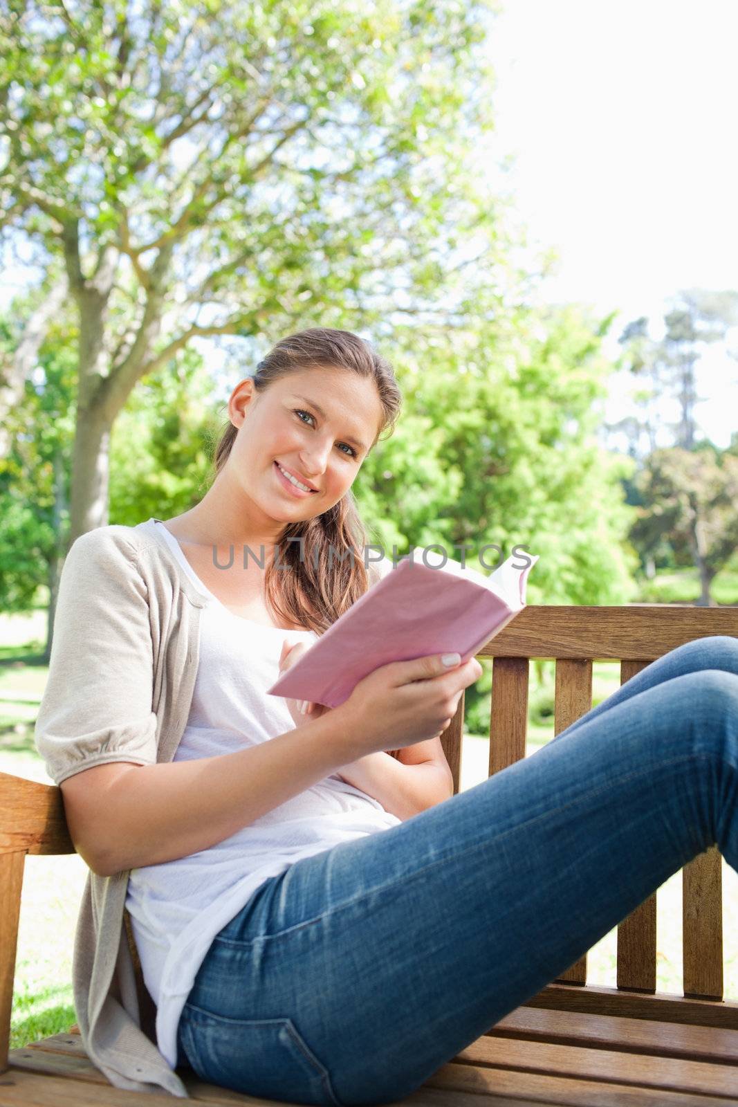 Smiling young woman sitting on a bench in the park with a book