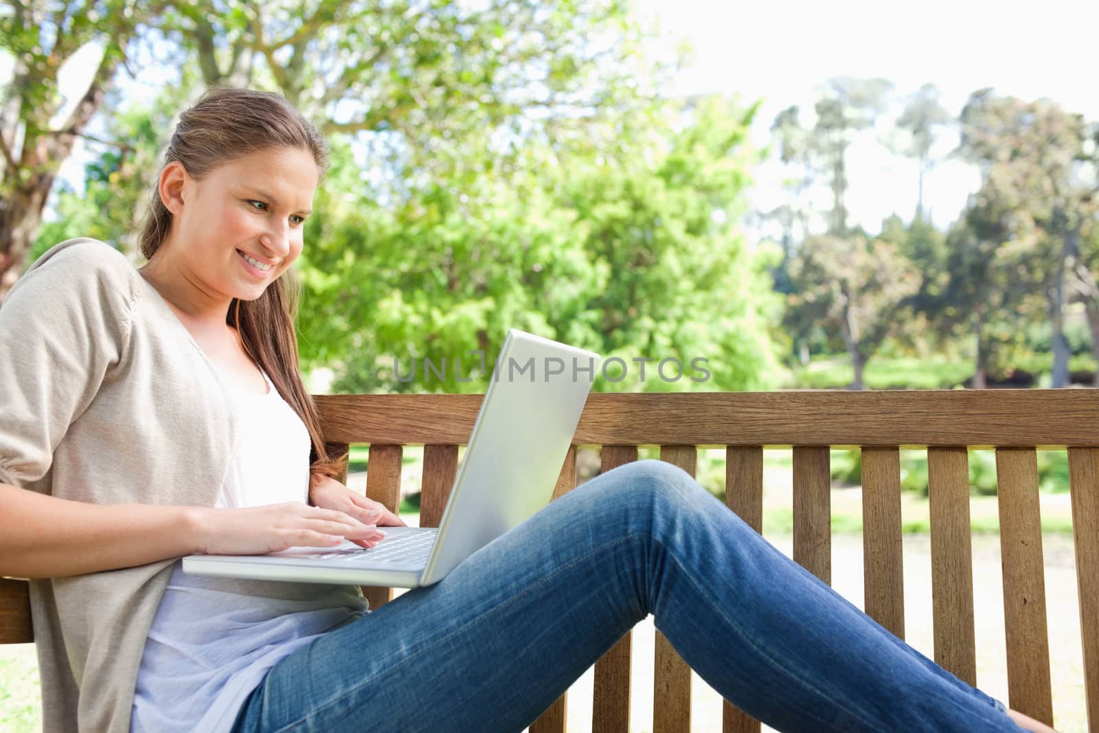 Side view of a smiling young woman on a bench with her laptop