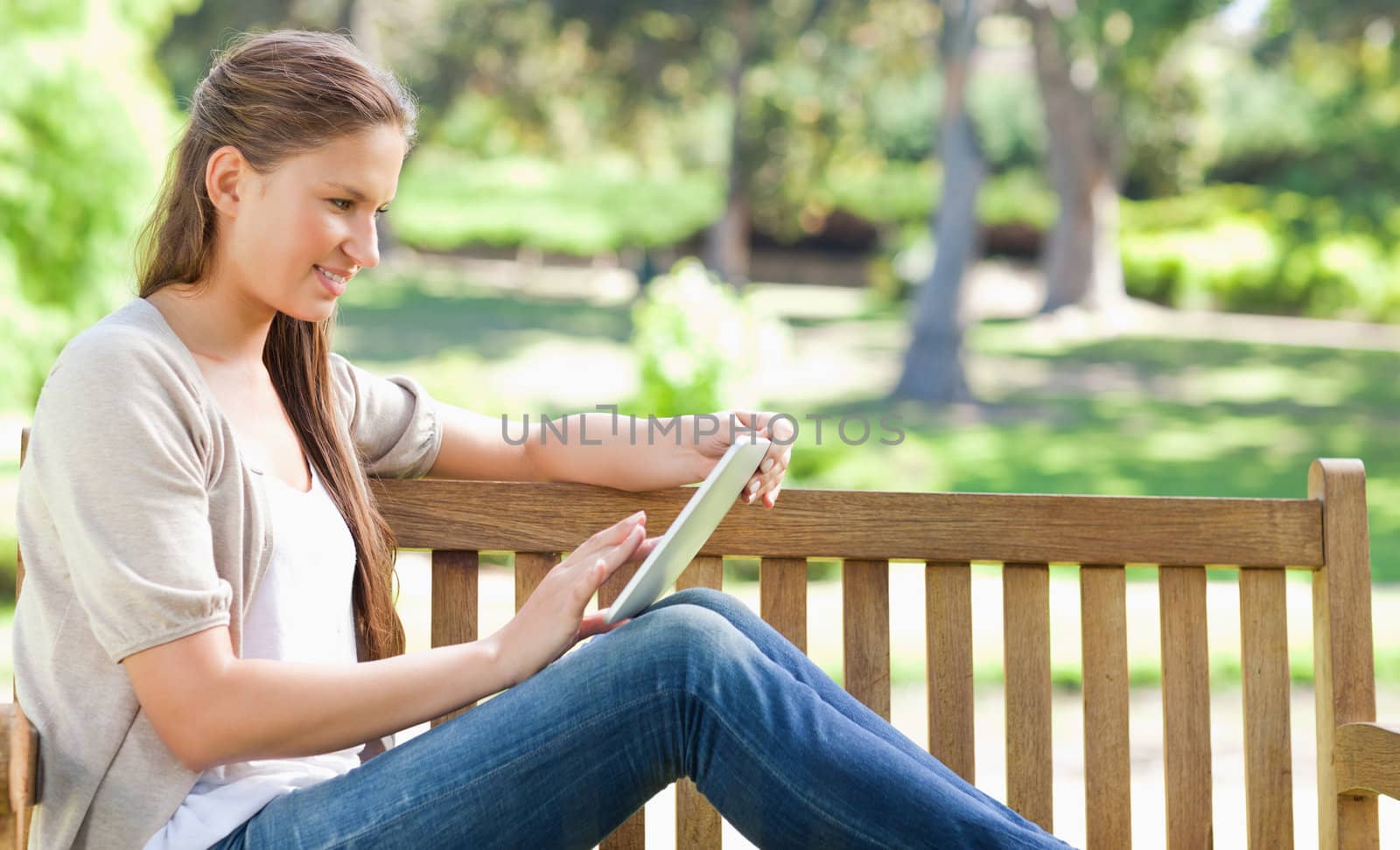 Side view of a young woman using a tablet computer on a park bench