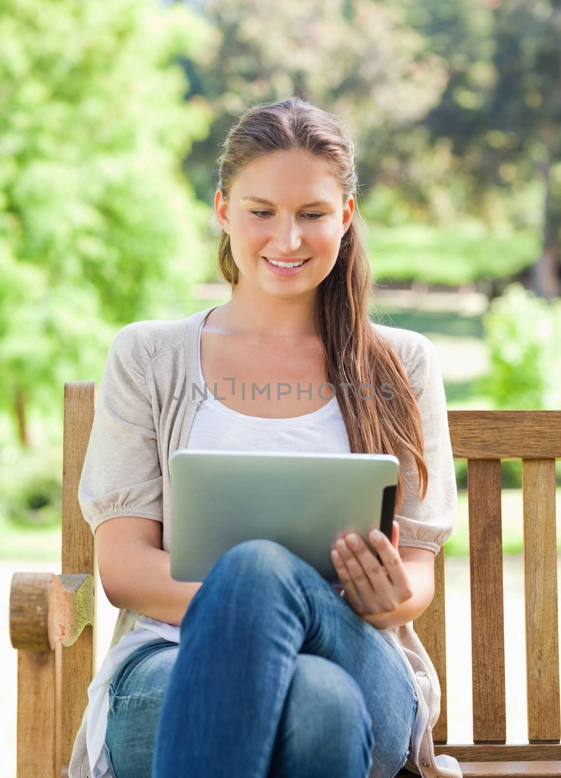 Smiling young woman using a tablet computer on a park bench