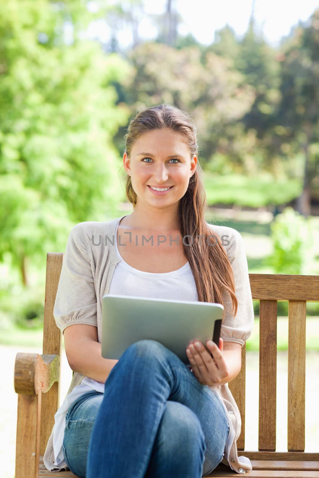 Smiling young woman on a park bench with a tablet computer