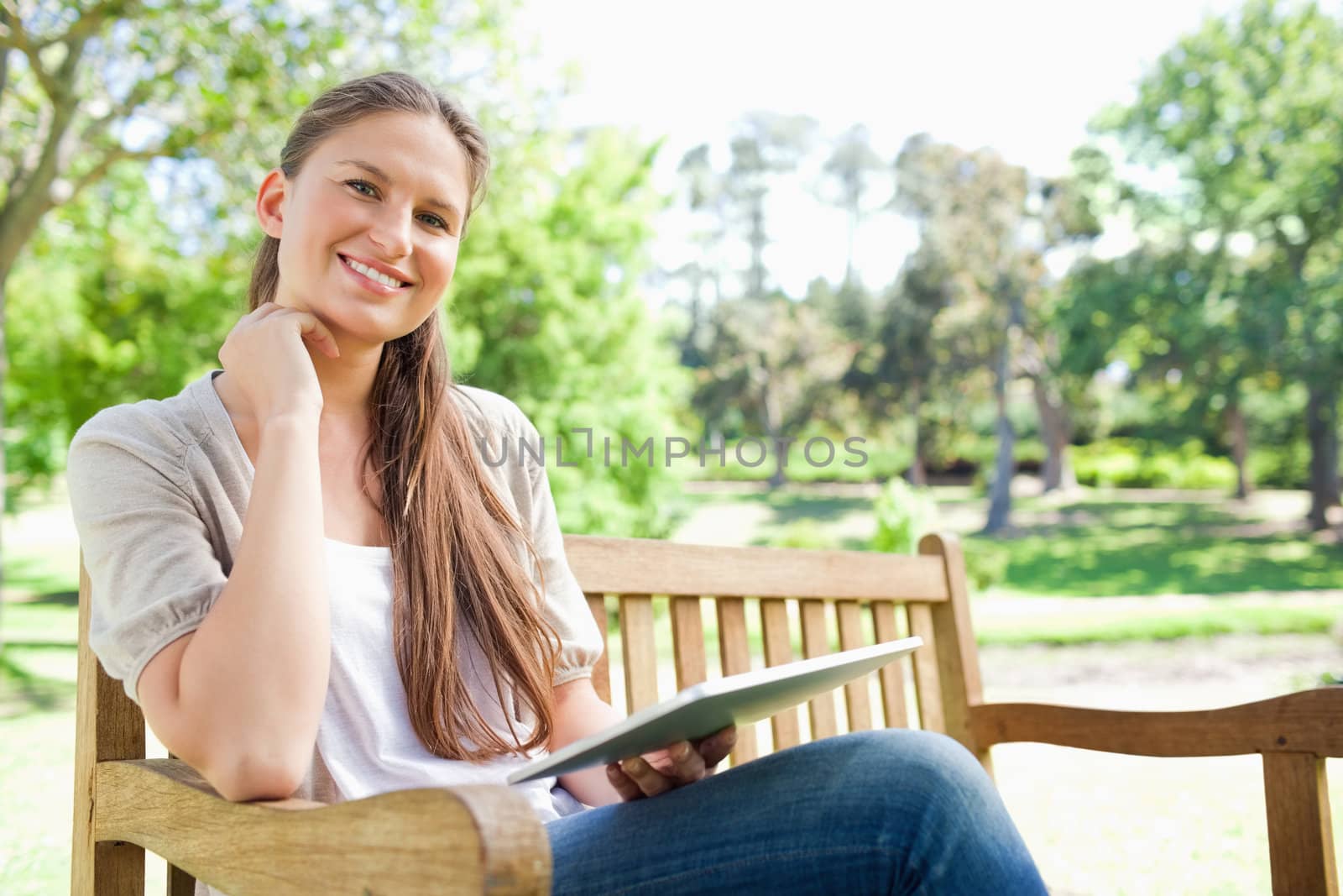 Smiling young woman on a park bench with her tablet computer