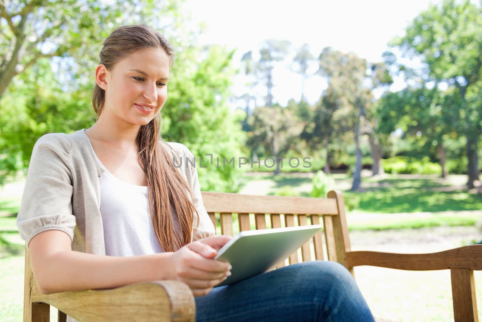 Smiling young woman using a tablet on a park bench