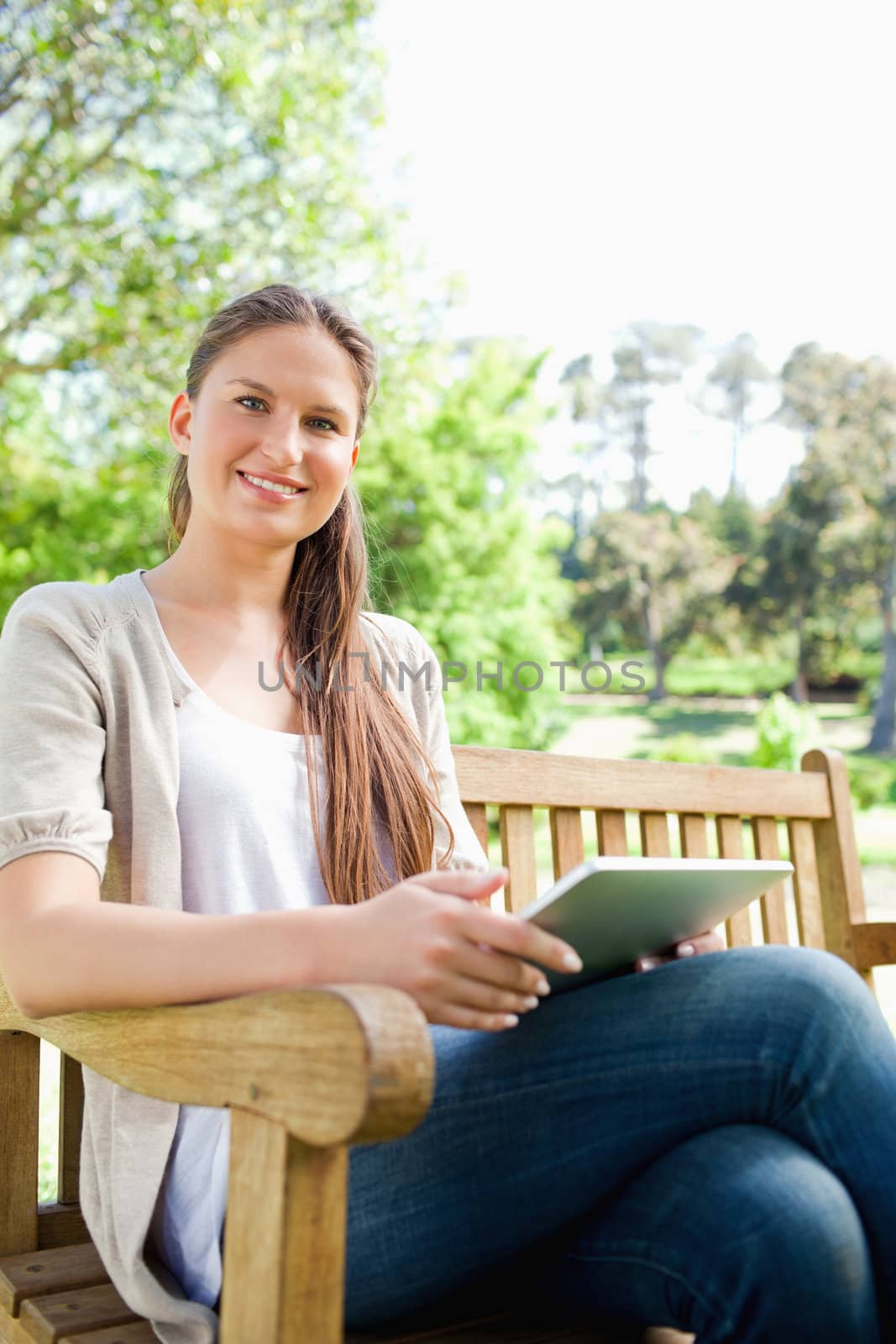 Smiling young woman sitting on a bench with her tablet computer