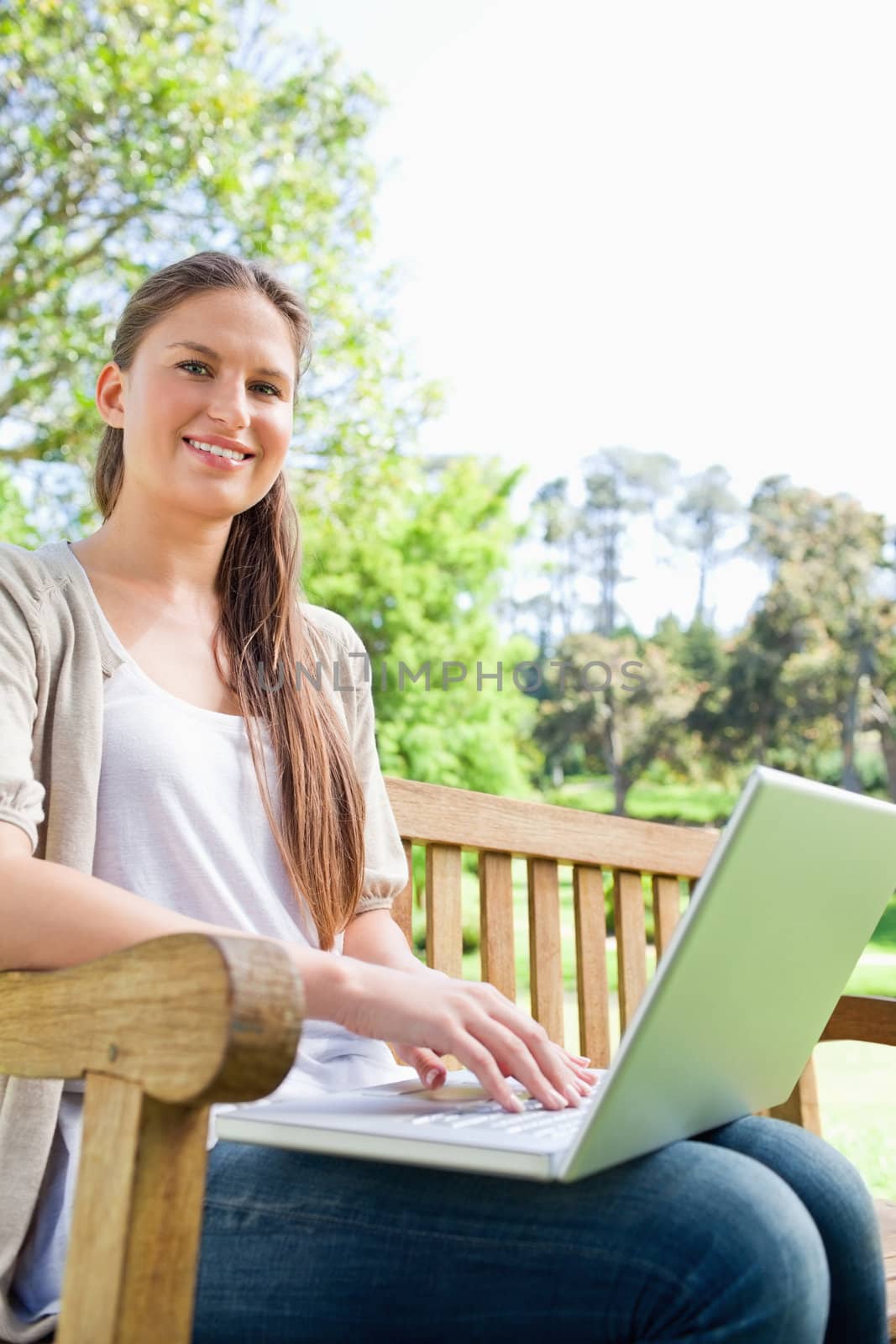 Smiling woman with her notebook sitting on a park bench by Wavebreakmedia