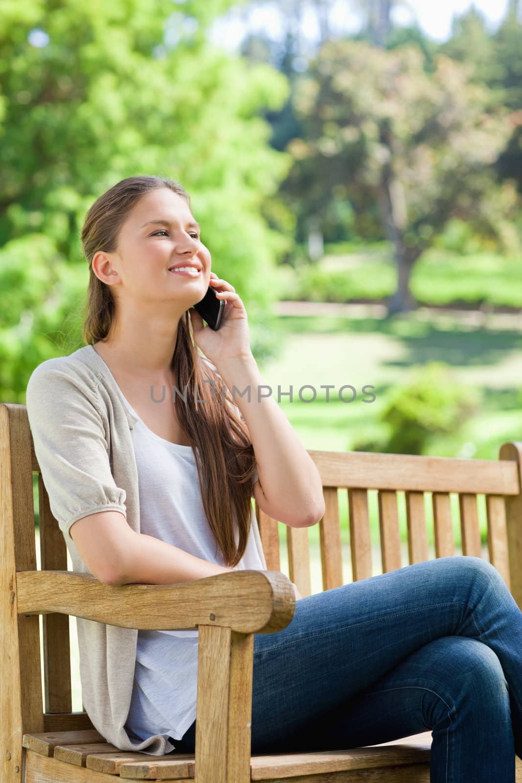Smiling young woman sitting with her cellphone on a park bench