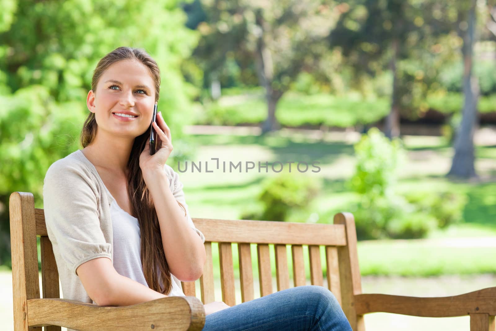 Smiling young woman on her cellphone while sitting on a park bench