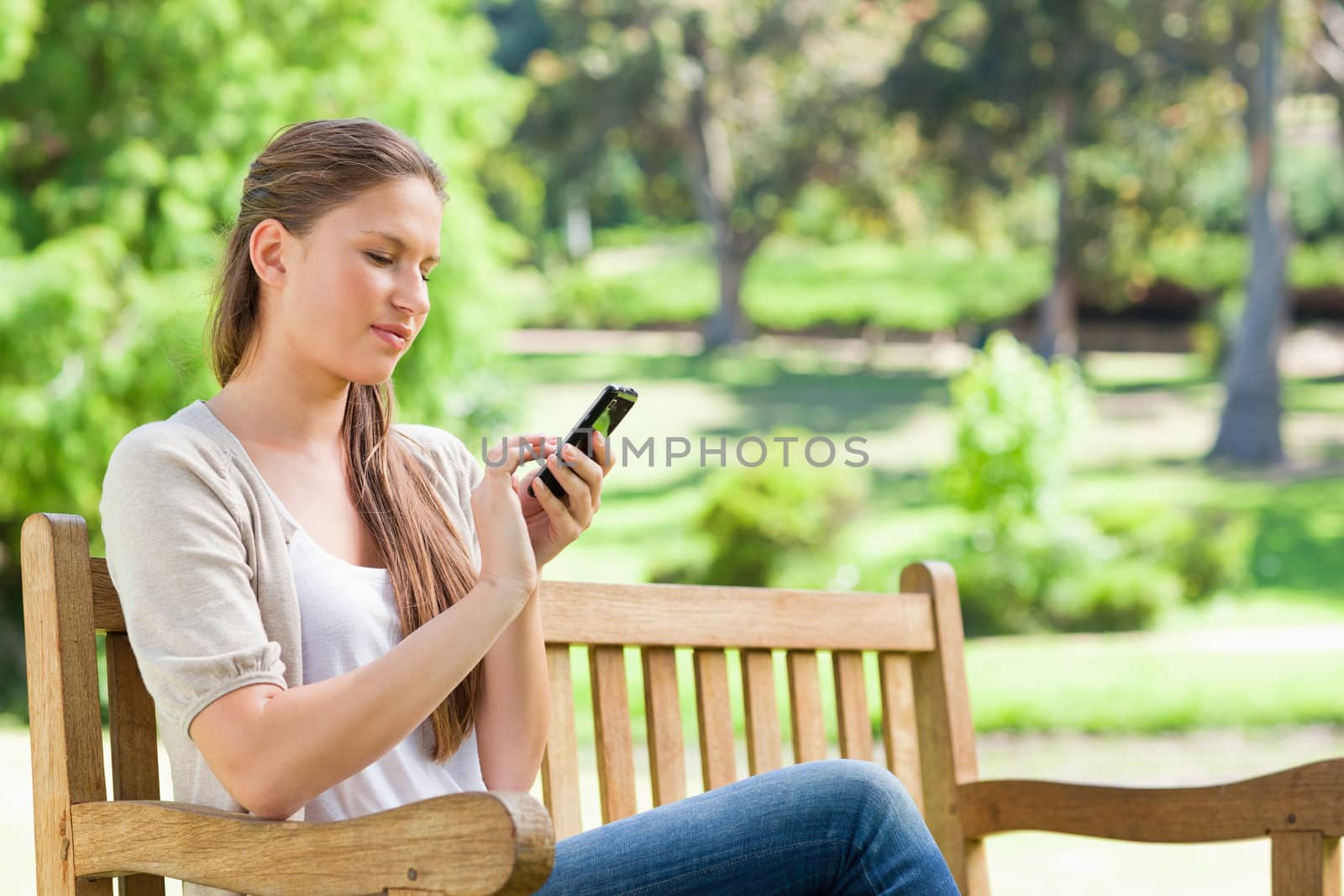 Young woman writing a text message on her cellphone while on a park bench