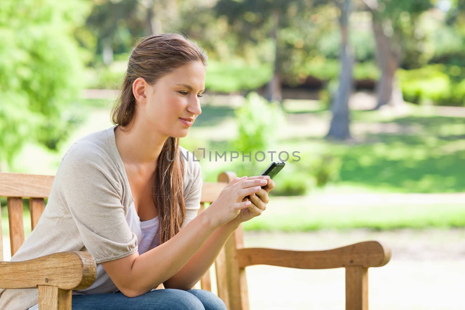 Woman reading a text message on a park bench by Wavebreakmedia