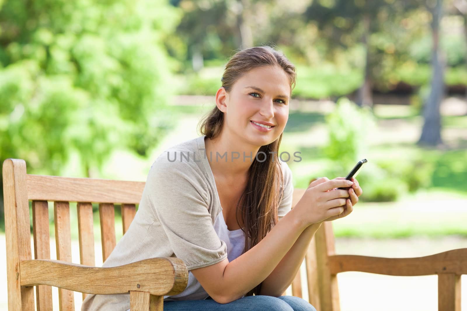 Smiling woman sitting on a park bench with her cellphone by Wavebreakmedia