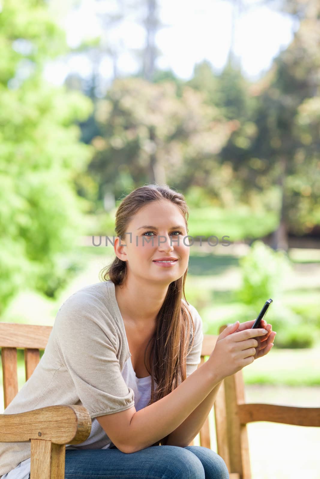 Smiling woman holding her cellphone while on a park bench by Wavebreakmedia