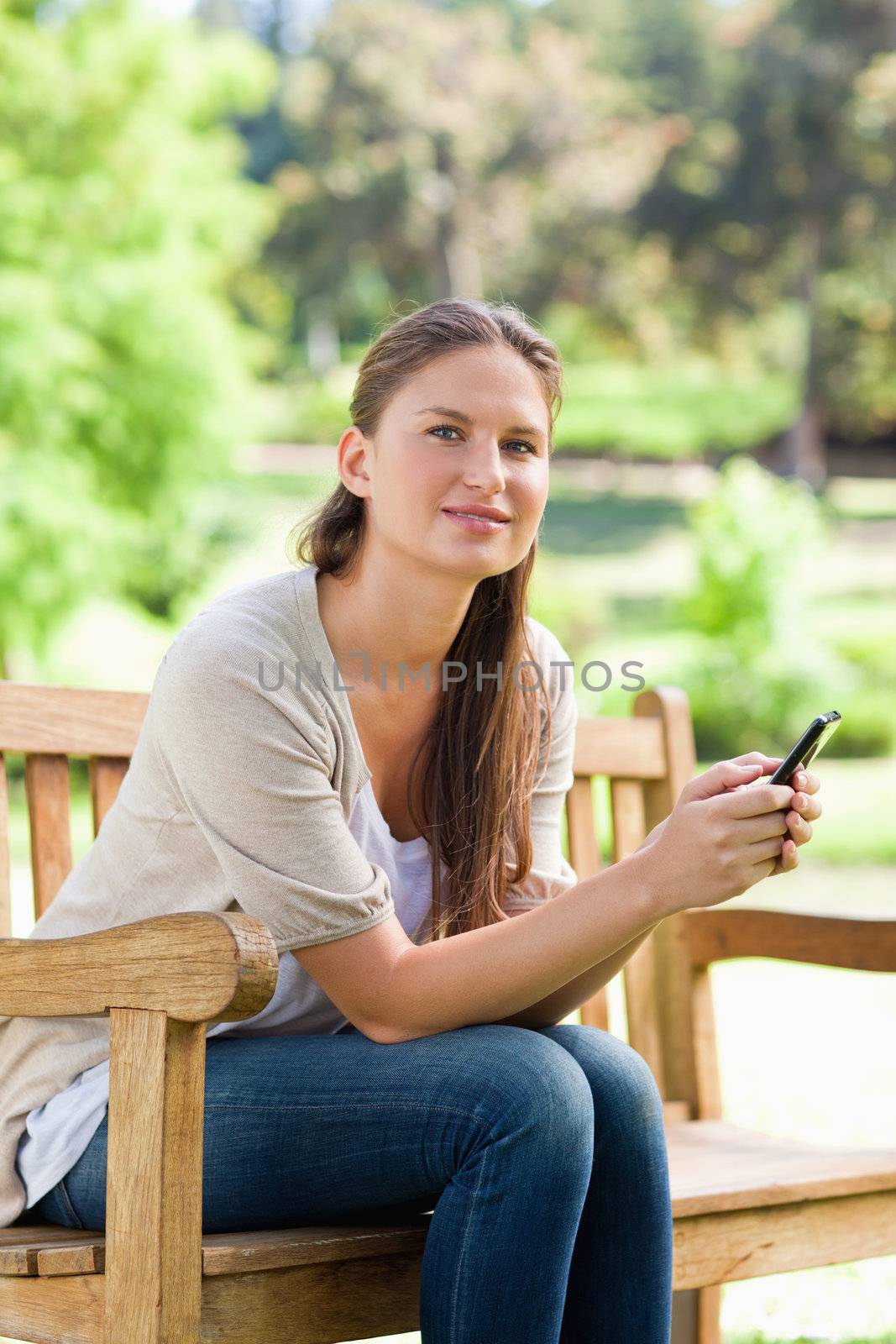 Woman with her cellphone sitting on a park bench by Wavebreakmedia