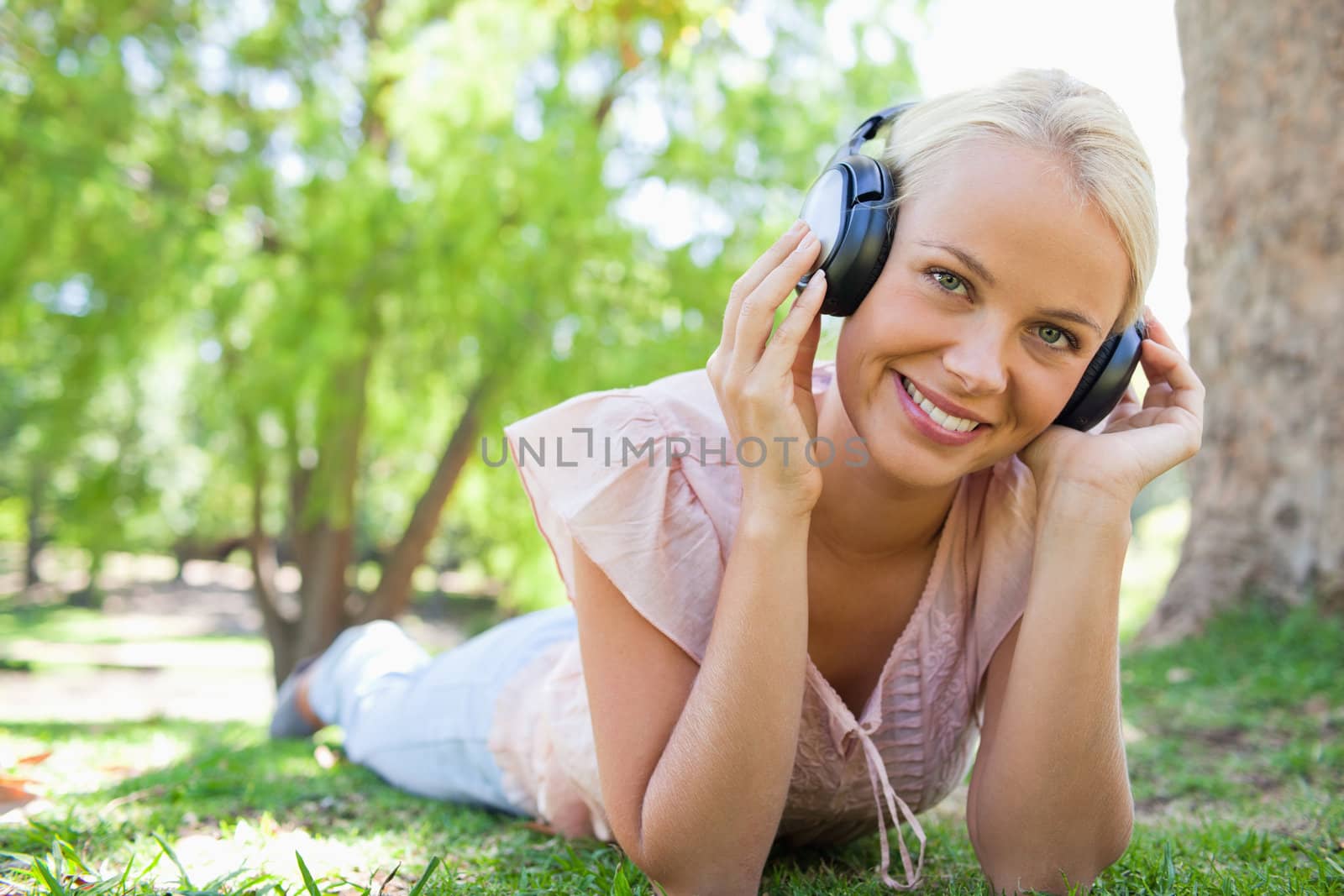 Smiling young woman lying on the grass while listening to music